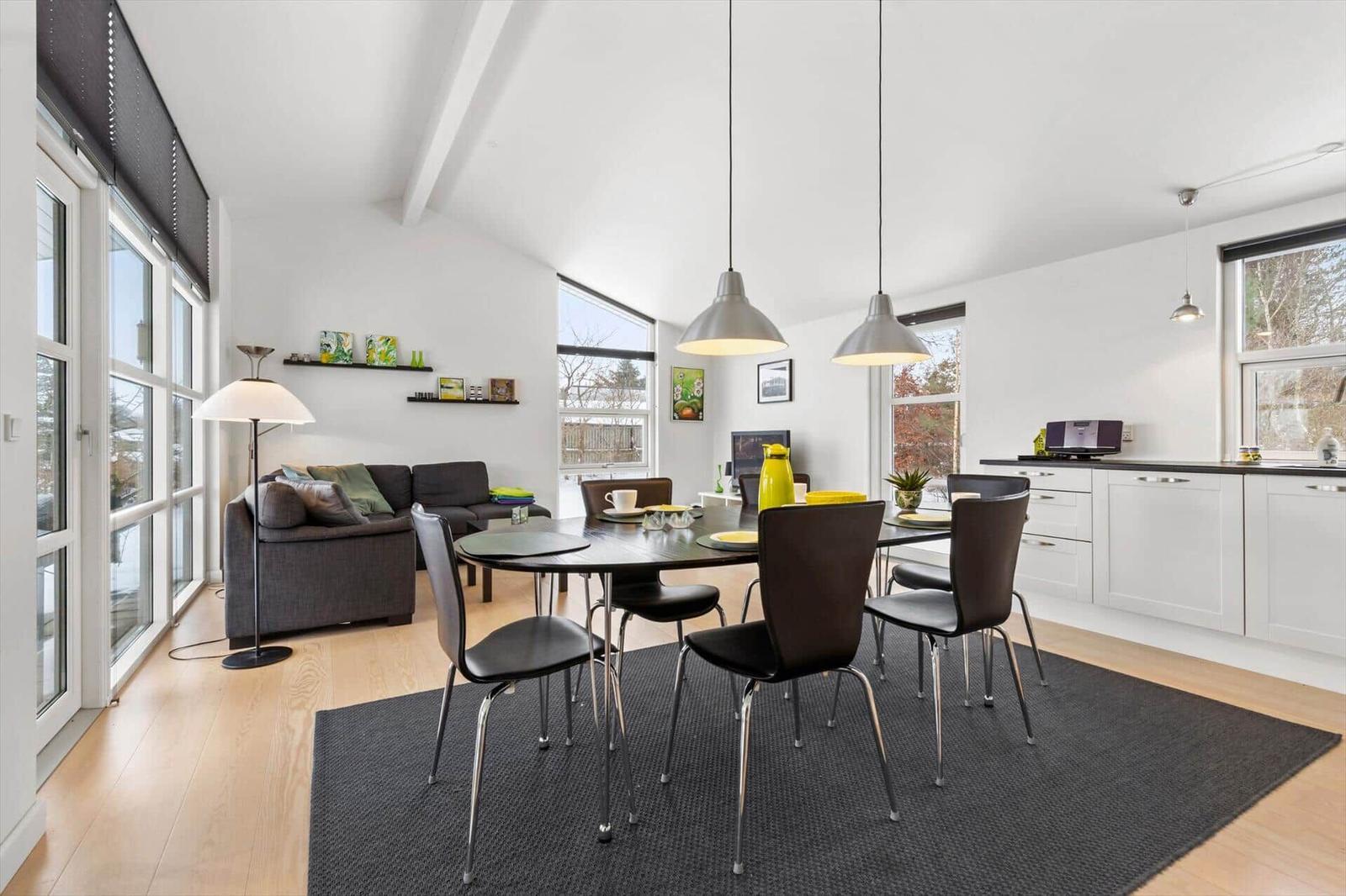 Living and dining area with table, chairs, and sofa. Windows and light walls.