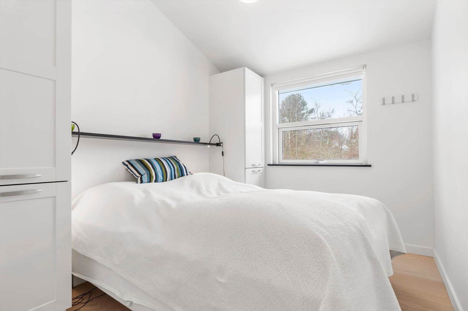 Bedroom with white bed, window, and white cabinets.