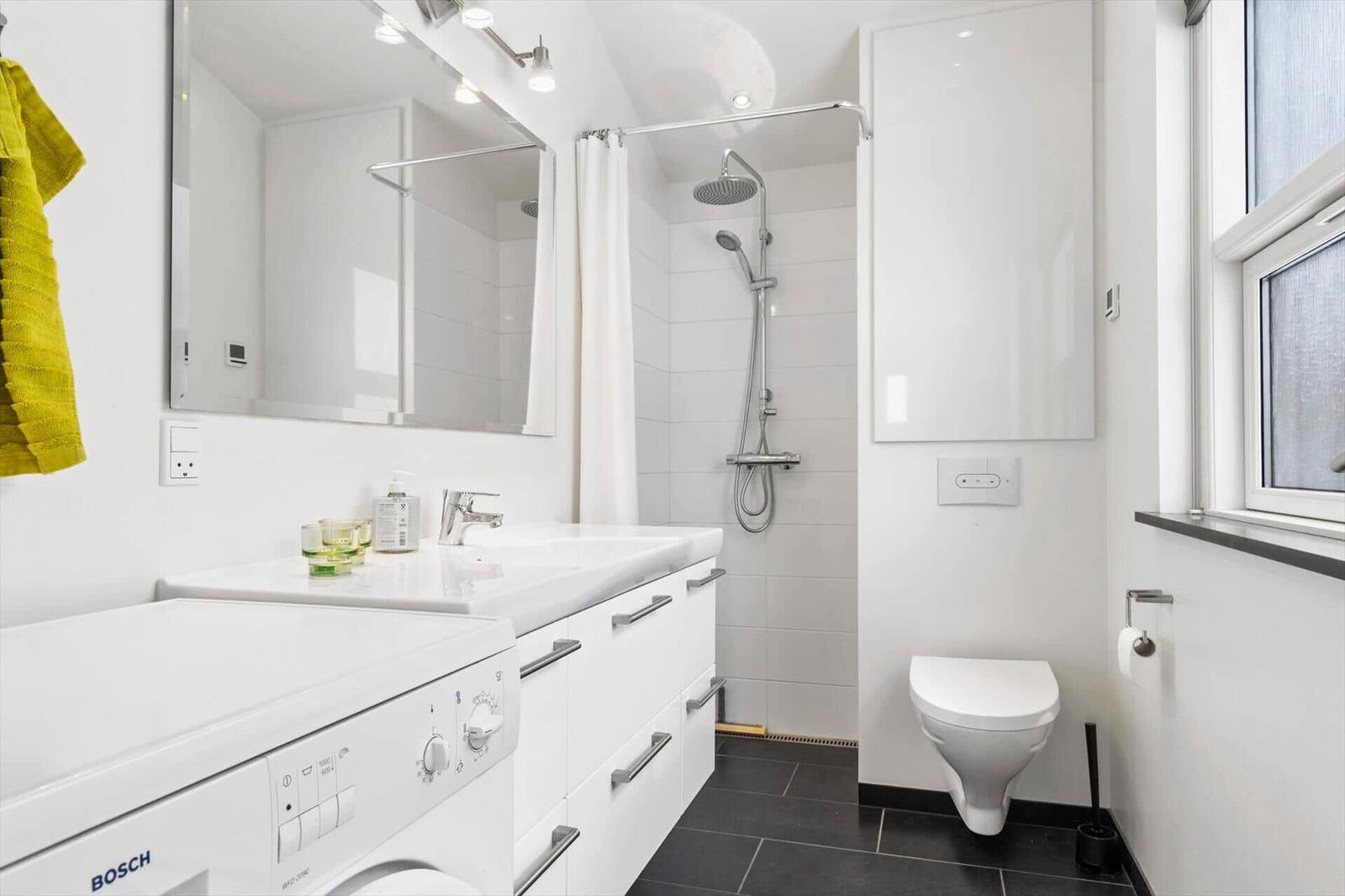 Bathroom with shower, sink, and toilet. White tiles and black floor tiles.