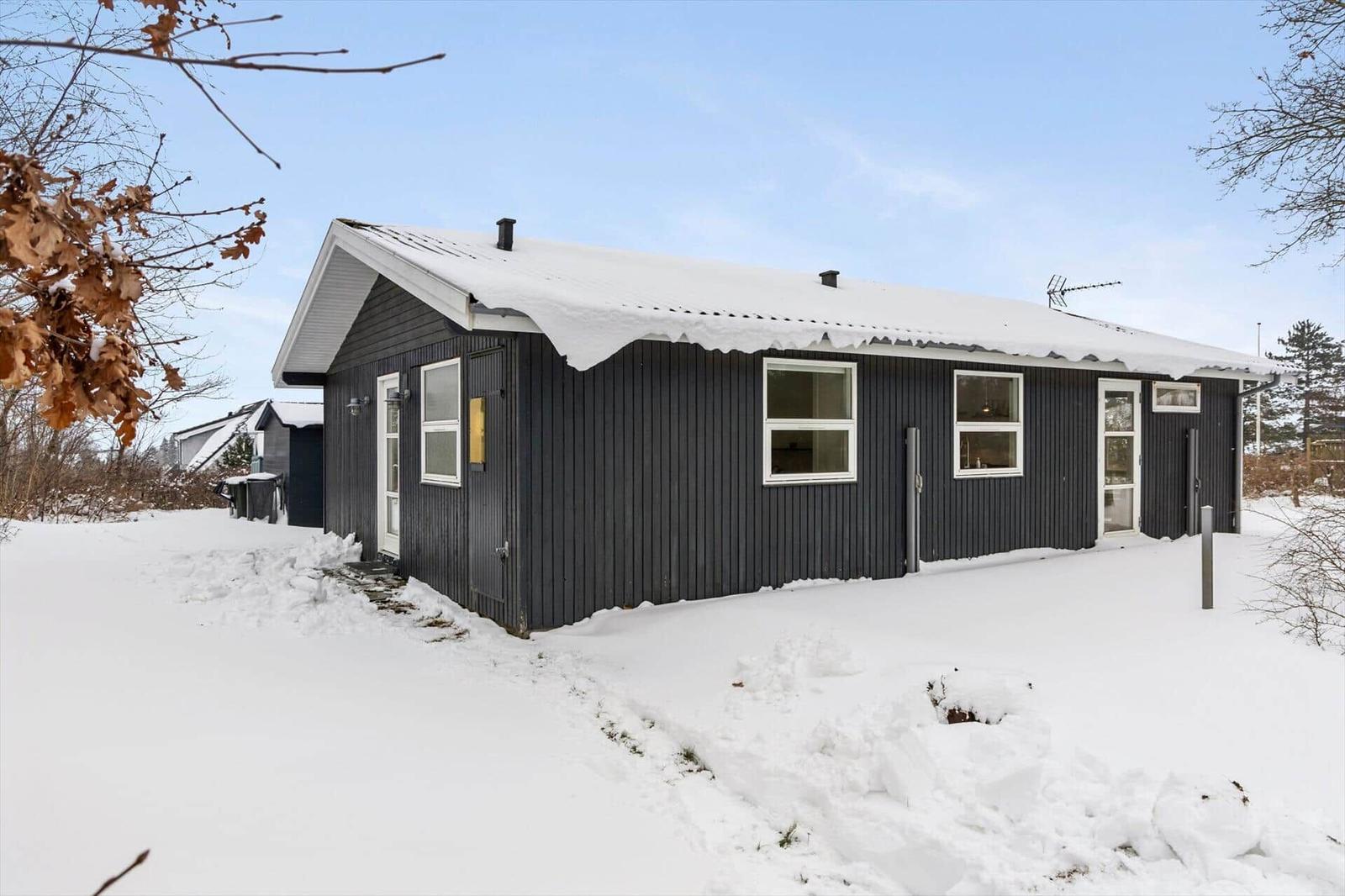 Black wooden house with snow-covered roof and white window frames.