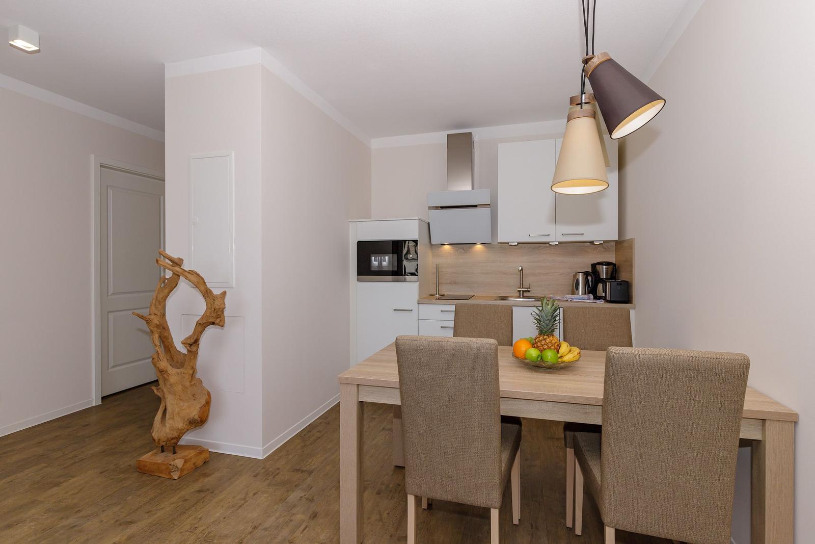 Essbereich mit Tisch, Stühlen und Küchenzeile. Dekorative Holzskulptur links.