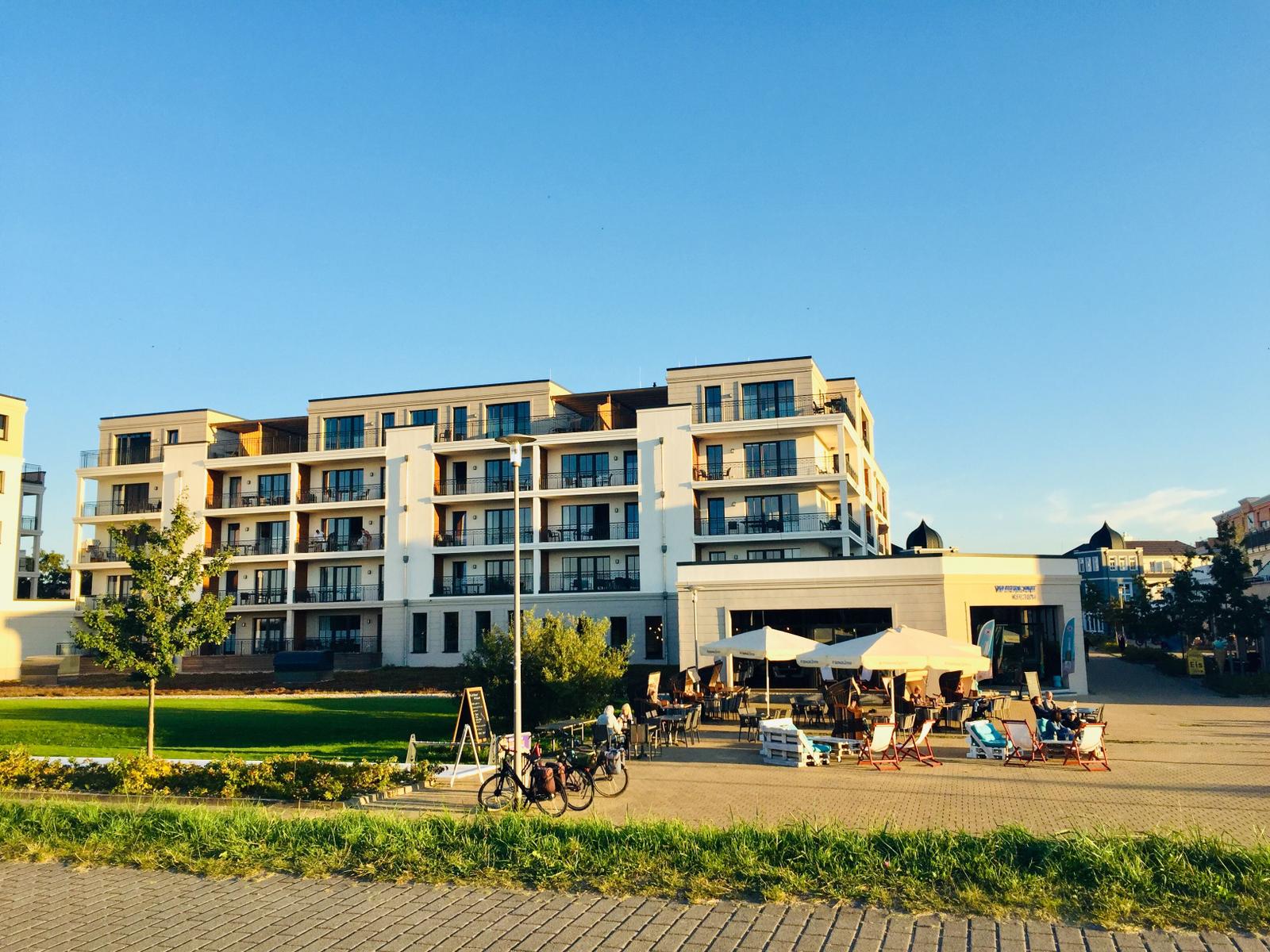 Modernes Mehrfamilienhaus mit Balkonen und Außenbereich mit Tischen und Stühlen.