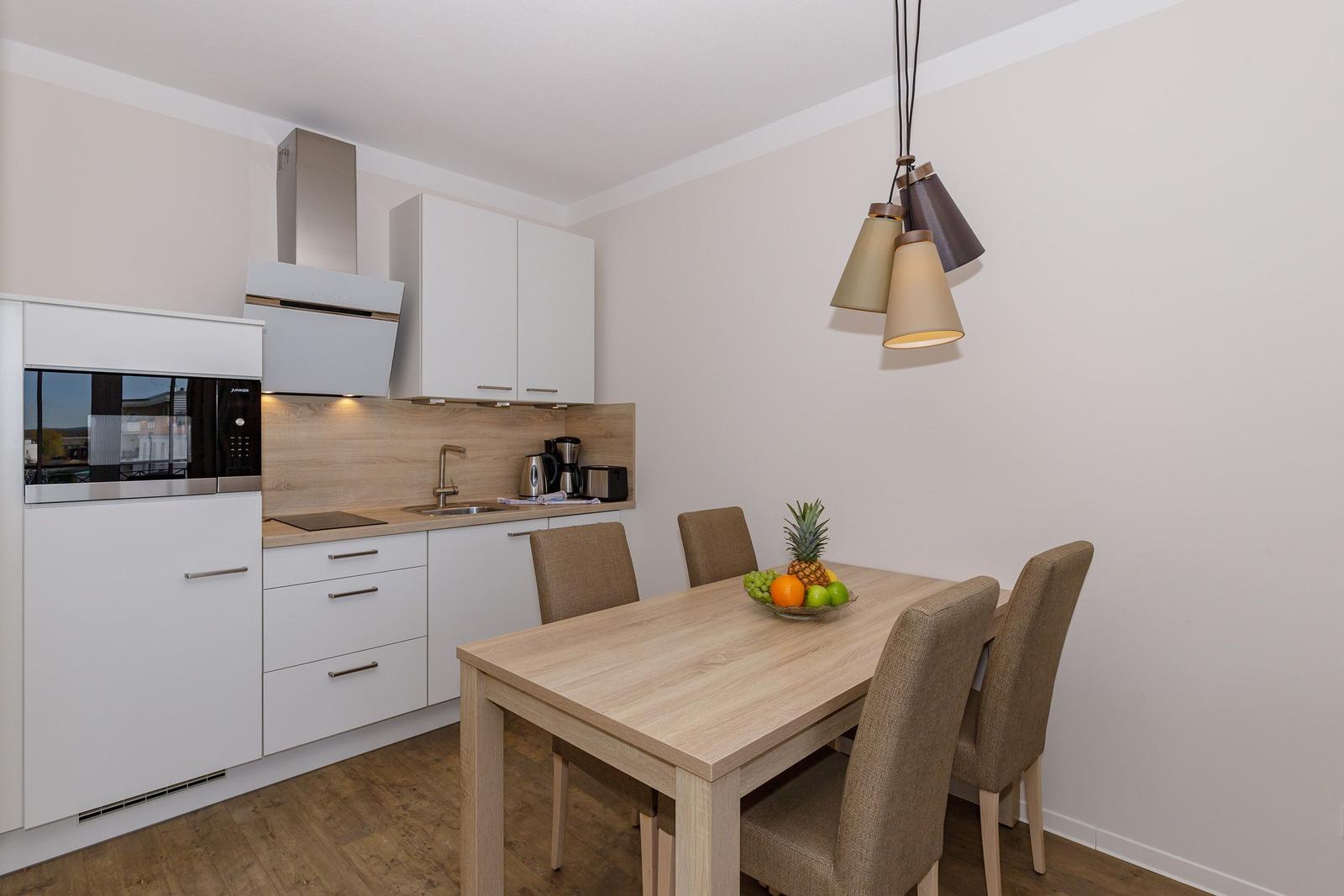 Küche mit Essbereich, Holztisch und vier Stühlen, moderne Einbauküche mit Dunstabzug.