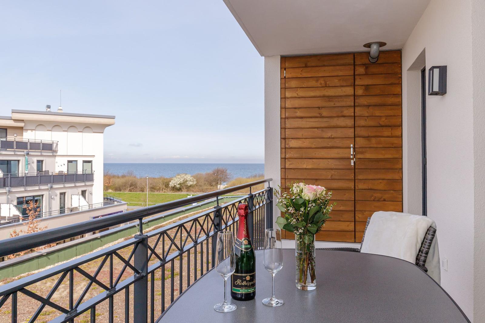 Balcony with table, glasses, and flowers overlooking the sea and buildings.