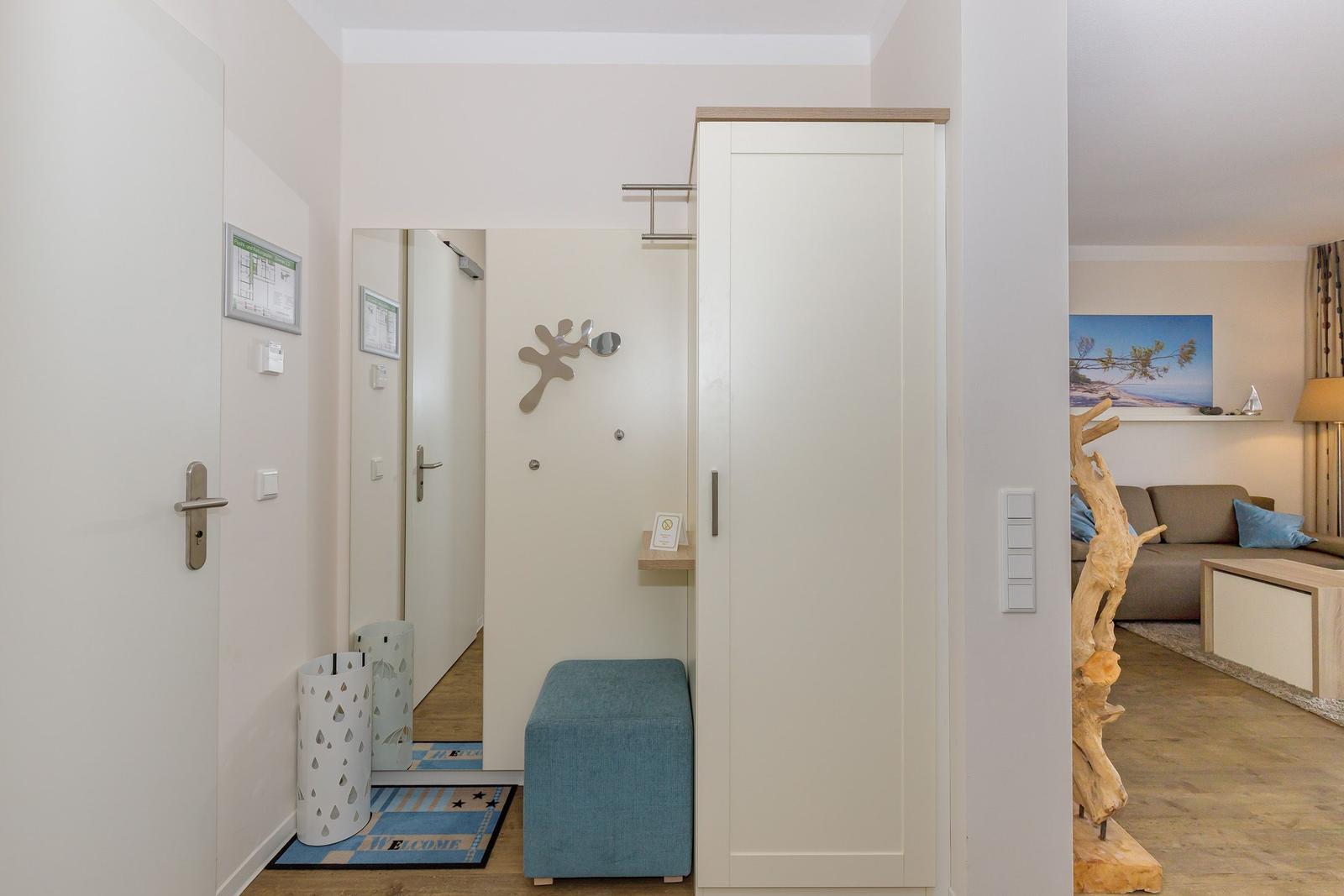 Eingangsbereich mit Garderobe, Sitzhocker und Blick in Wohnzimmer mit Sofa.