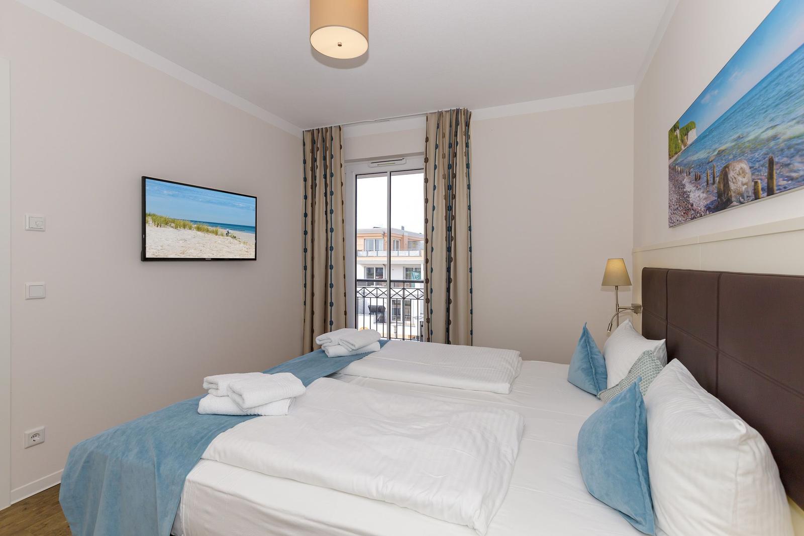 Schlafzimmer mit Doppelbett, TV und Balkonansicht.