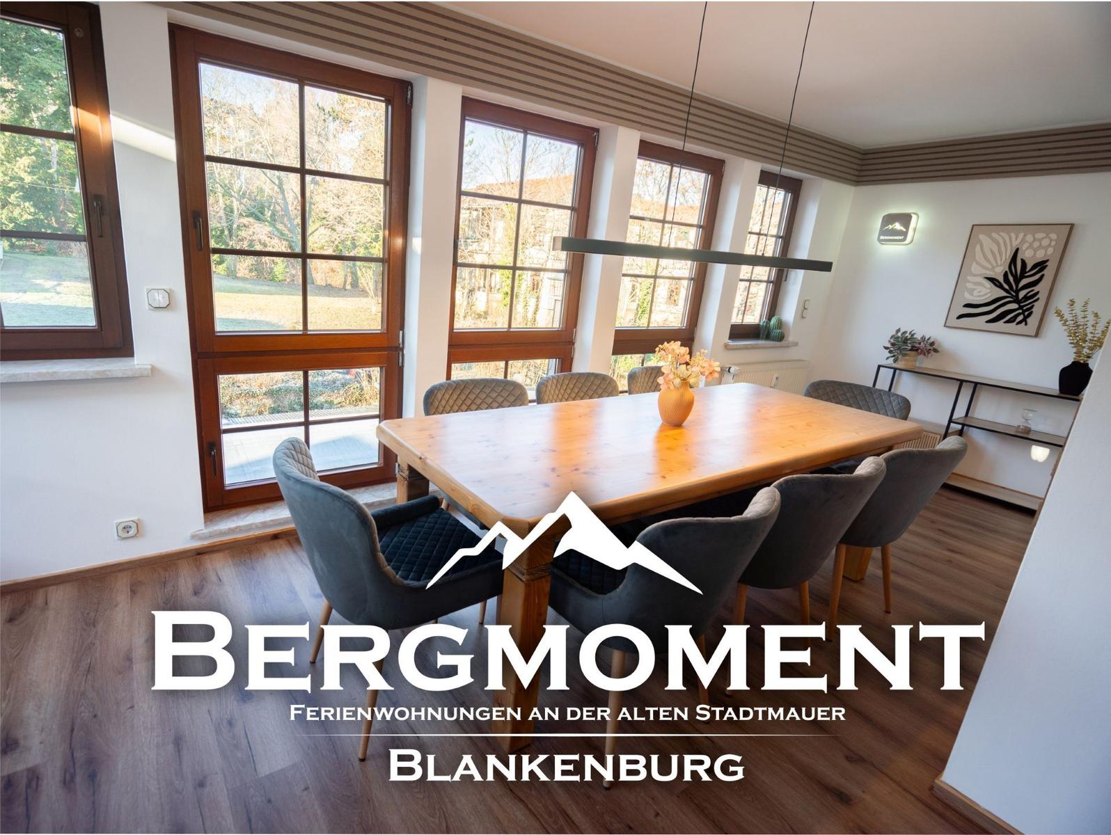 Esszimmer mit Holztisch, Stühlen und großen Fenstern zur Außenseite.