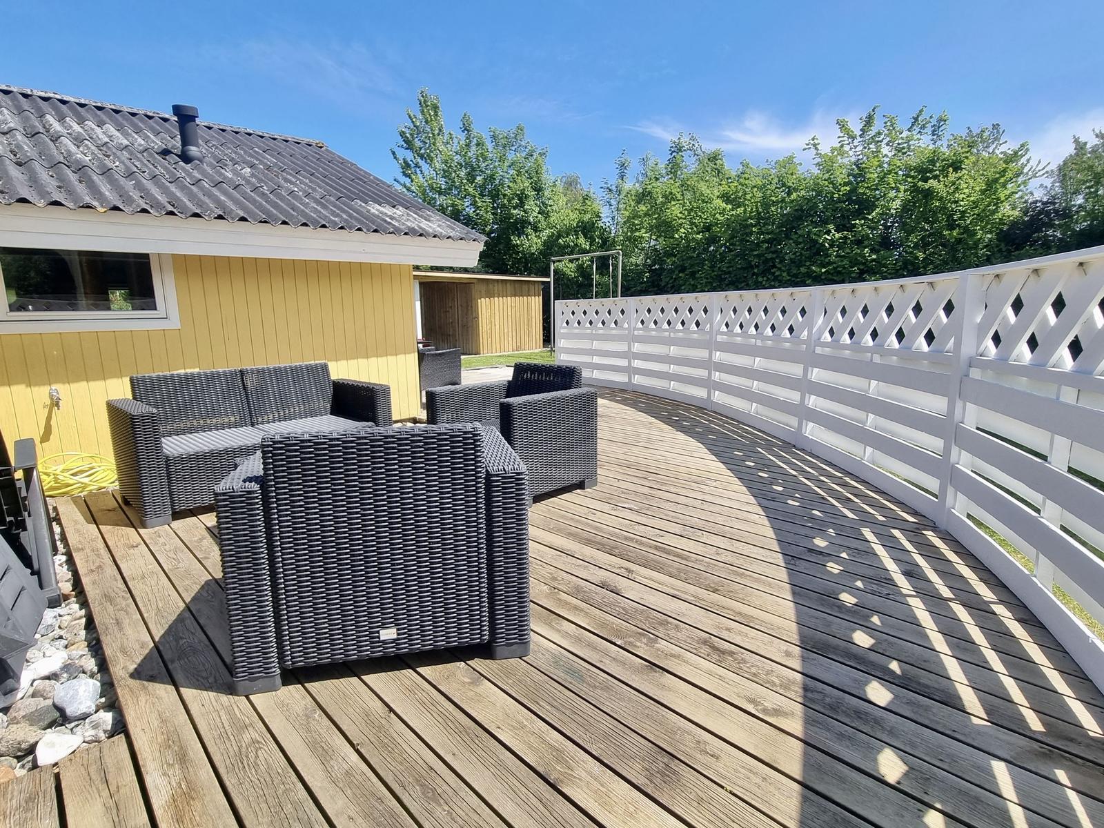 Terrasse mit Gartenmöbeln und weißem Zaun. Hintergrund: gelbes Haus und Bäume.
