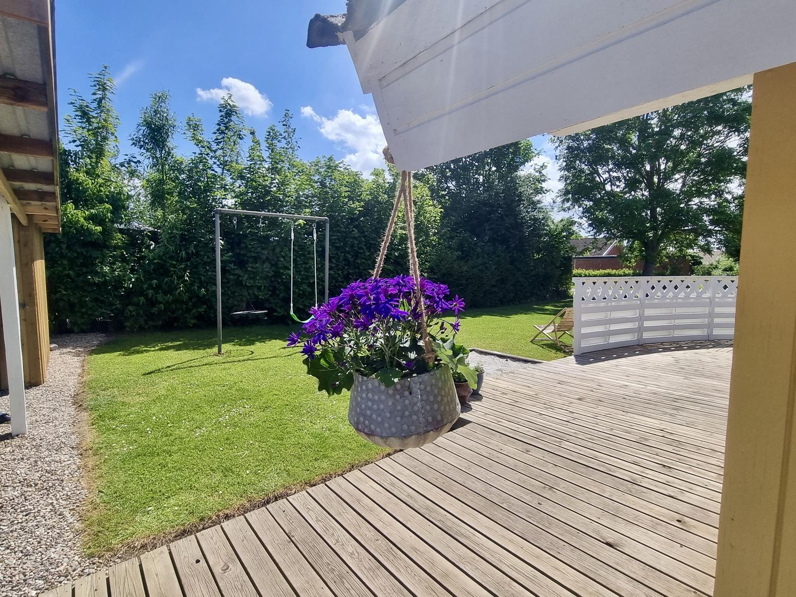 Terrasse mit Blumenkorb, Spielgerüst und grünem Rasen im Hintergrund.