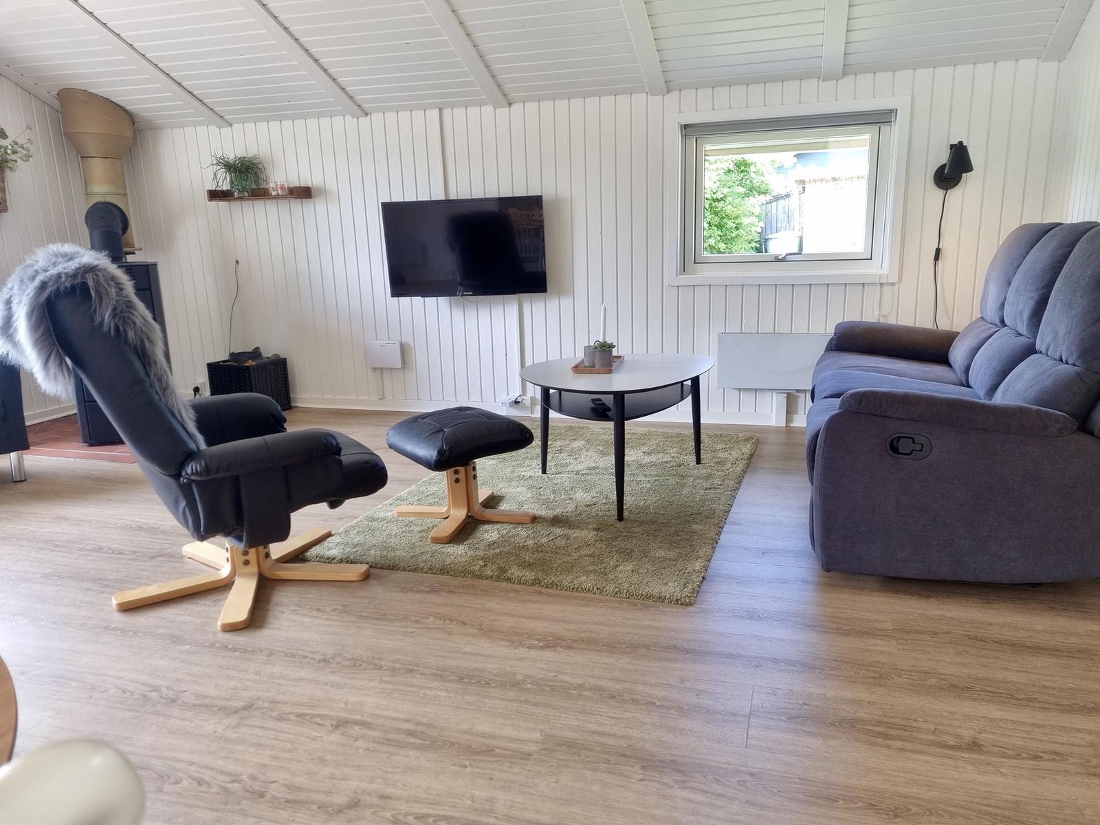 Wohnzimmer mit Sofa, Sessel, TV und Fenster.