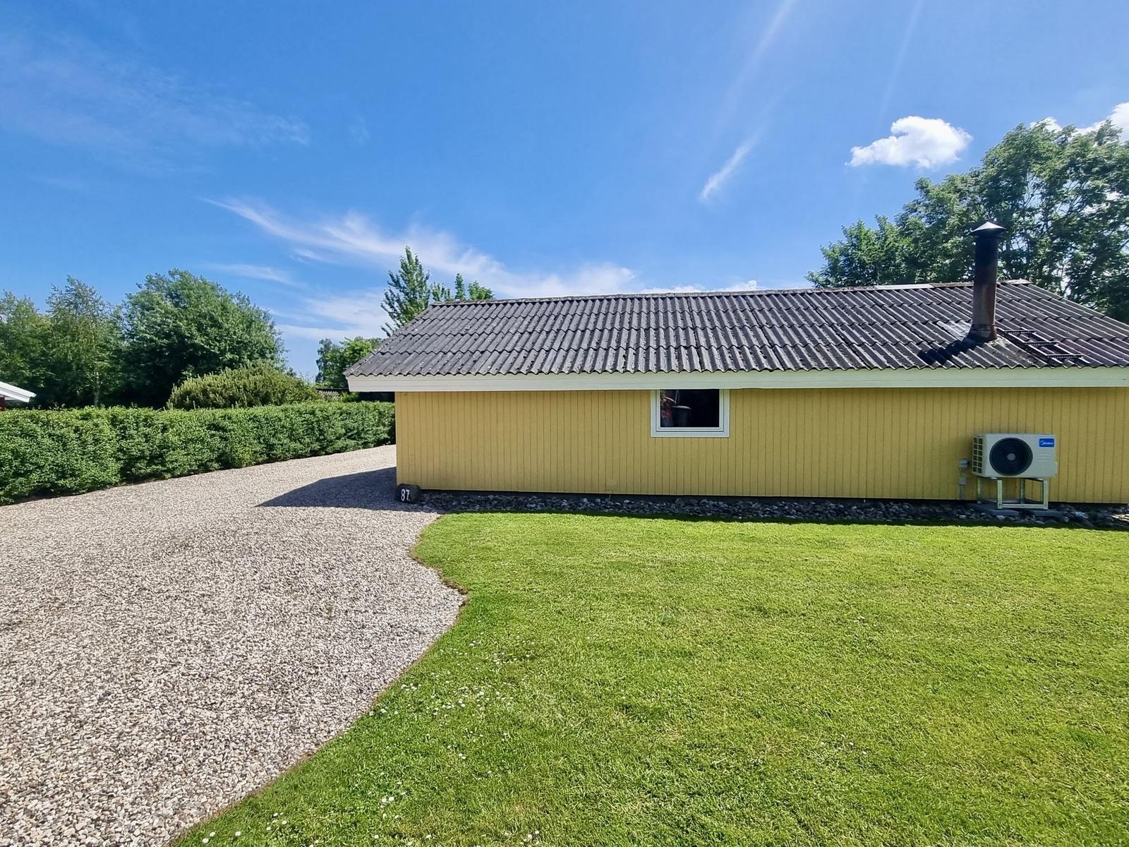 Gelbes Haus mit Schopf und Kamin, umgeben von Rasen und Gras.