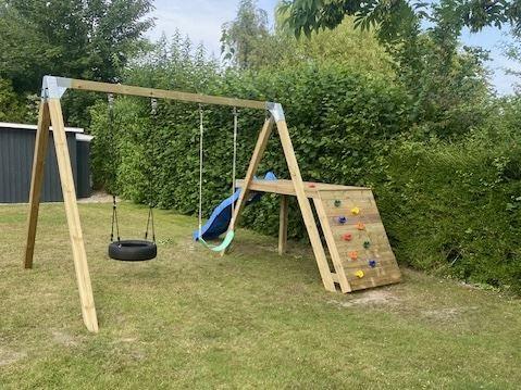 Holzspielgerüst mit Rutsche, Kletterwand und Reifen-Schaukel im Garten.