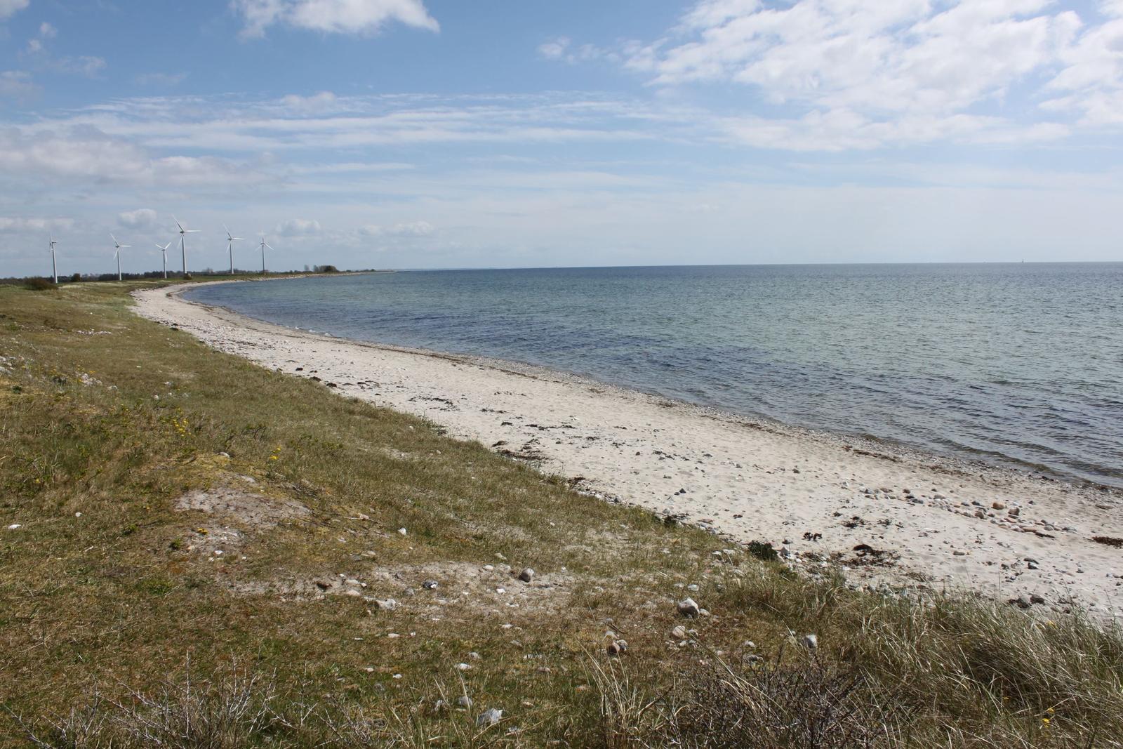 Strand mit Kiesstrand und Windrädern im Hintergrund