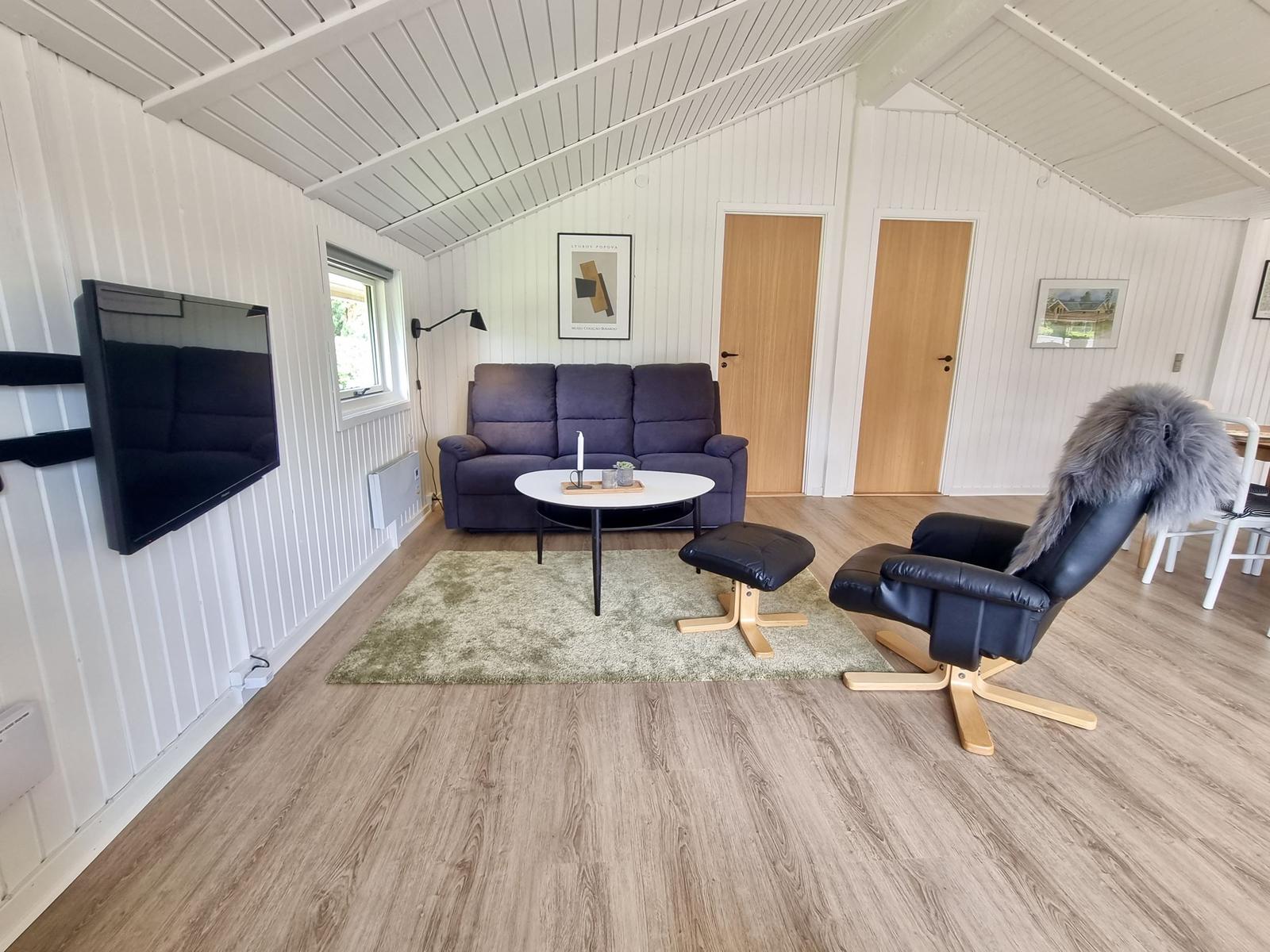 Wohnzimmer mit Sofa, Fernseher und Sessel auf Holzboden.