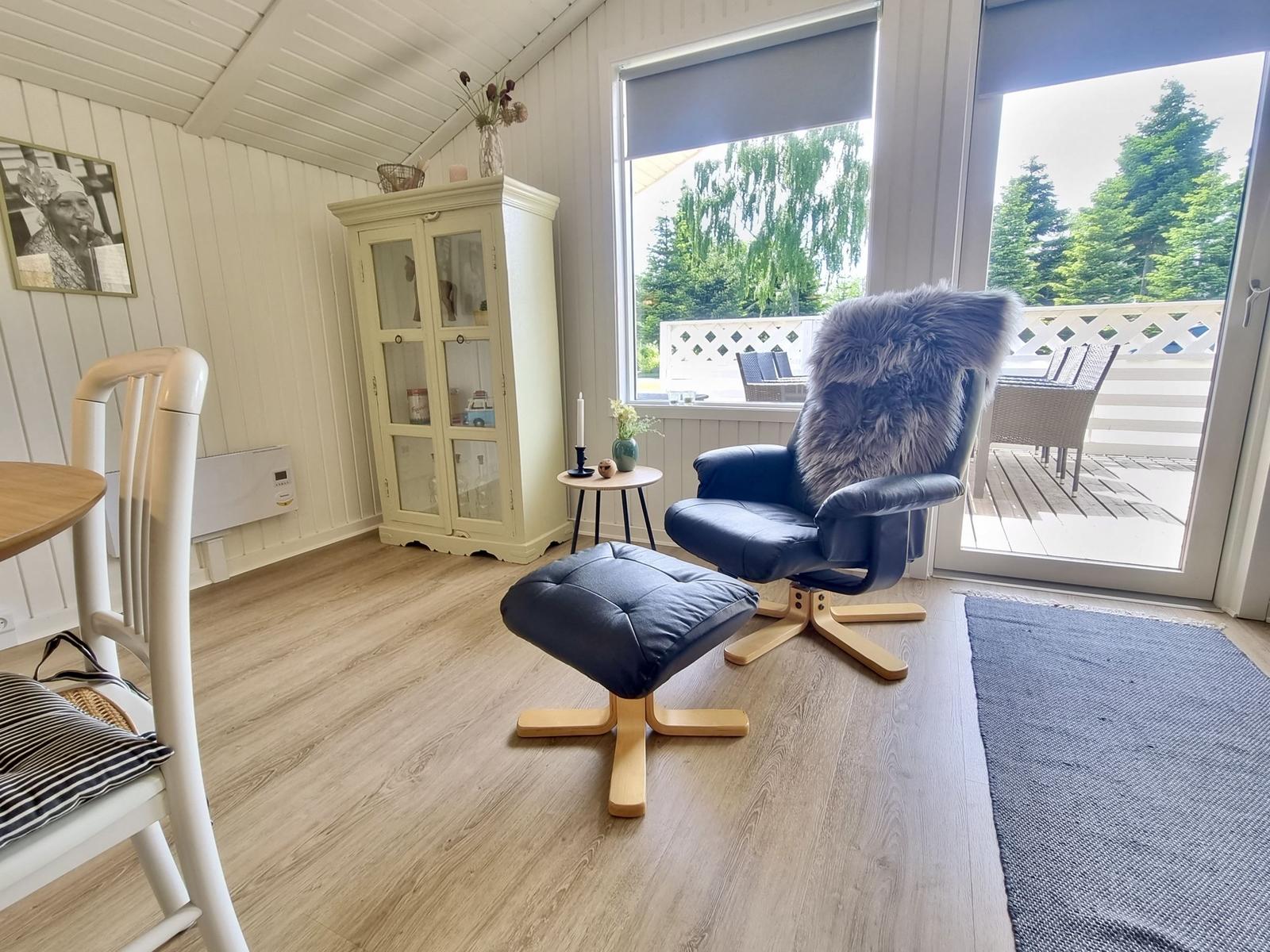 Ein Raum mit blauem Sessel, Holzboden und Blick auf die Terrasse.