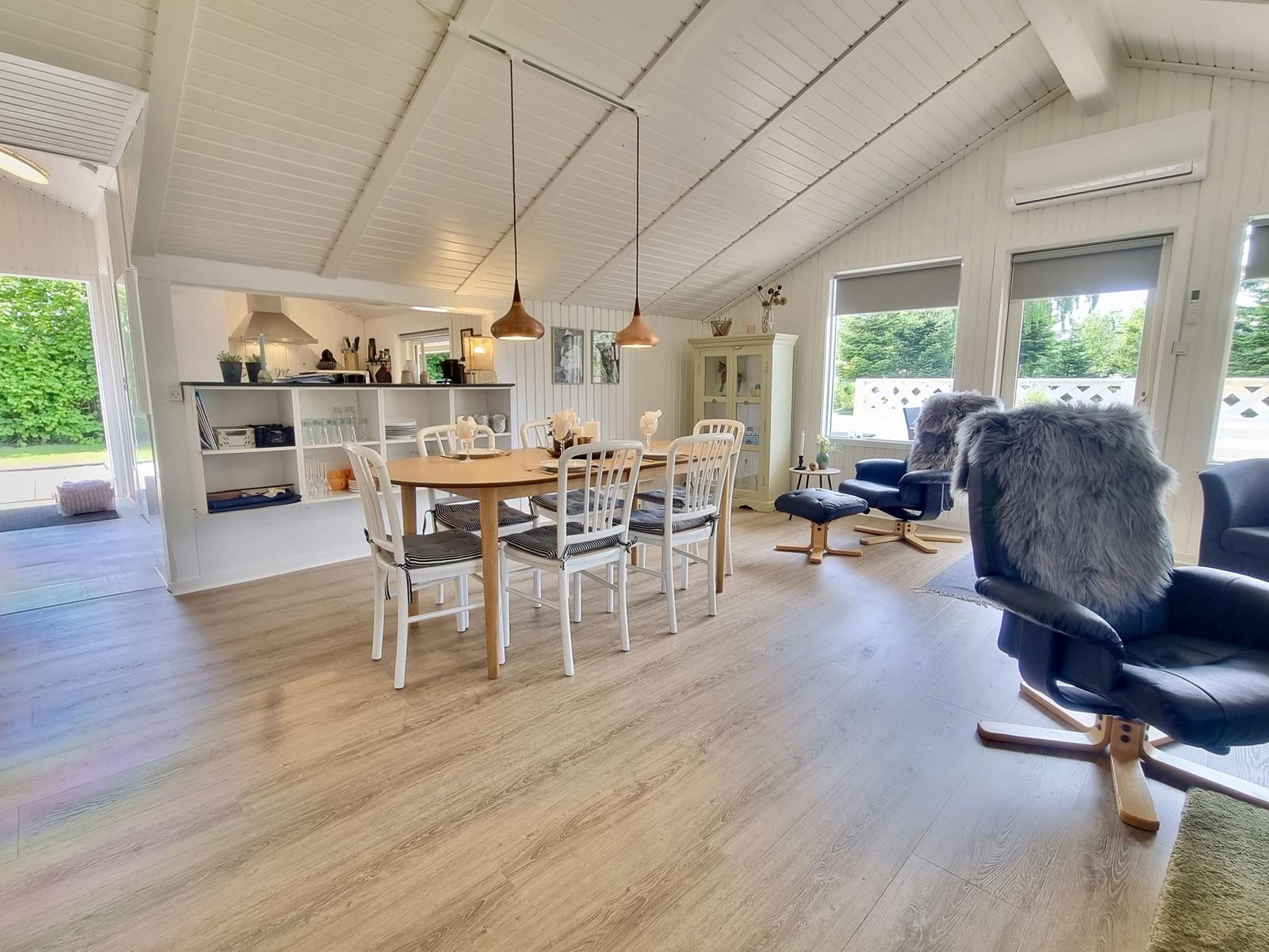 Essbereich mit Tisch und Stühlen, Sitzgelegenheiten und Küchenbereich im Hintergrund.