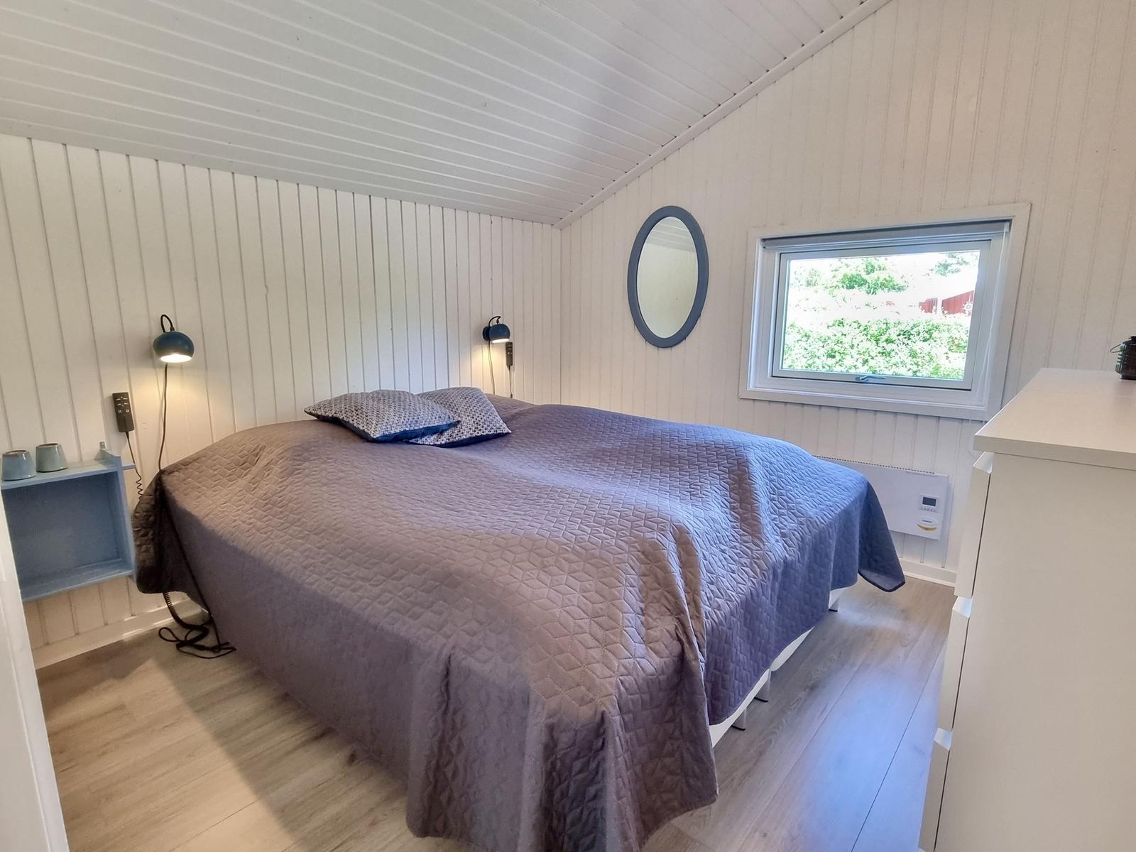 Schlafzimmer mit Bett, Fenster und Spiegel an der Wand.