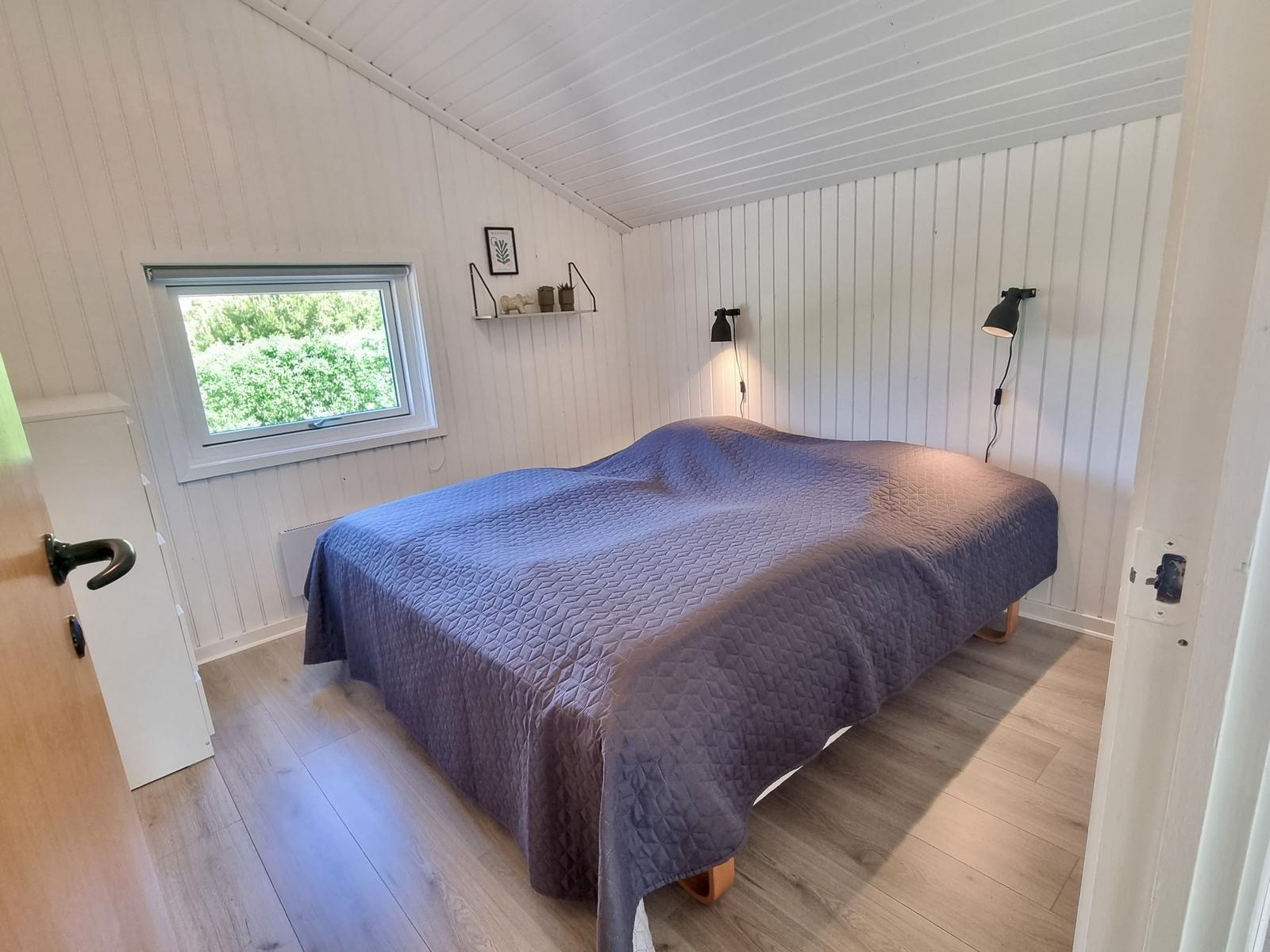 Schlafzimmer mit Bett, Fenster und Wandlampen.