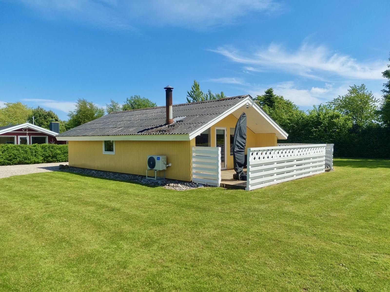 Gelbes Ferienhaus mit Terrasse und Garten unter blauem Himmel.