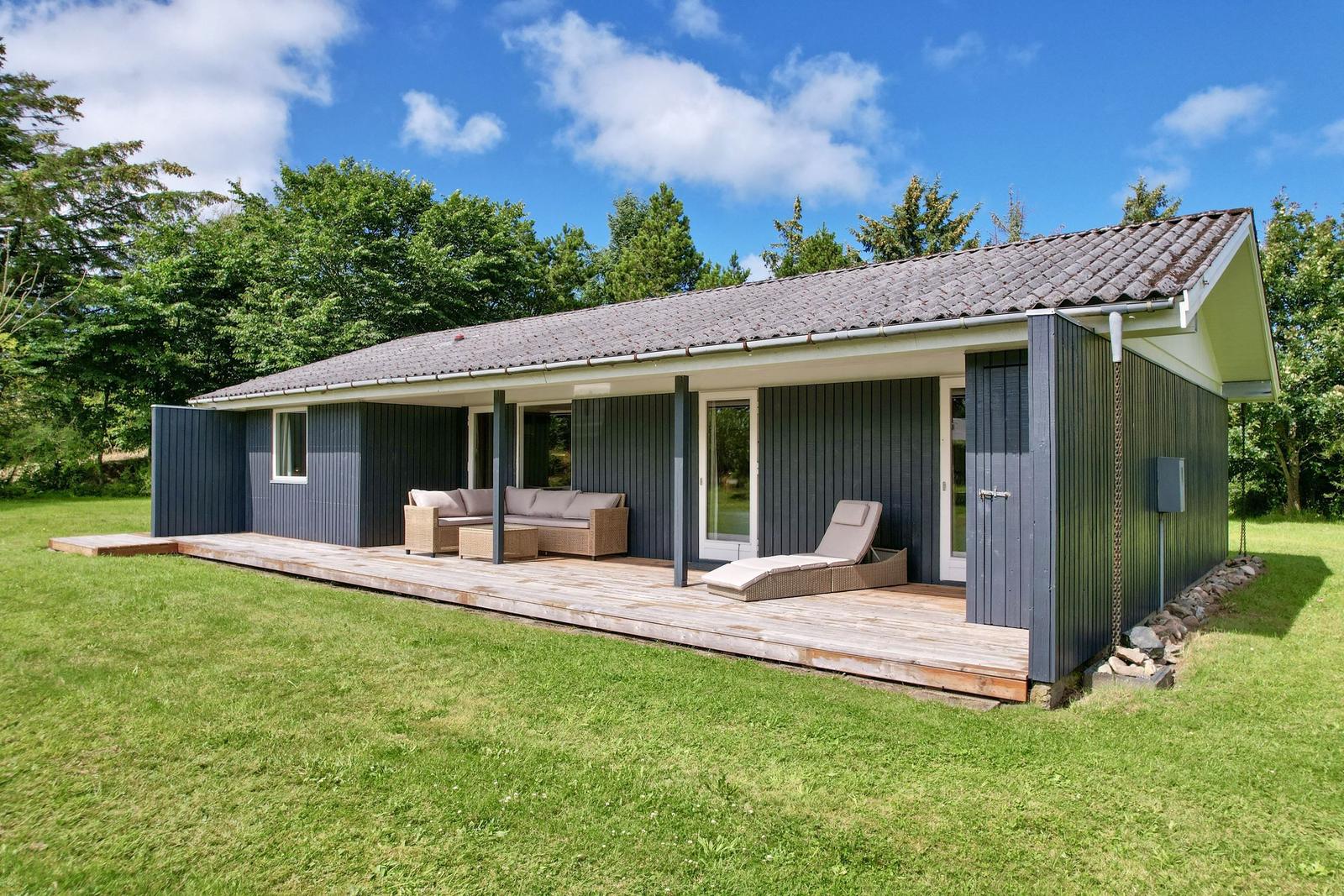 Ein modernes Haus mit Holzterrasse und Gartenmöbeln unter blauem Himmel.