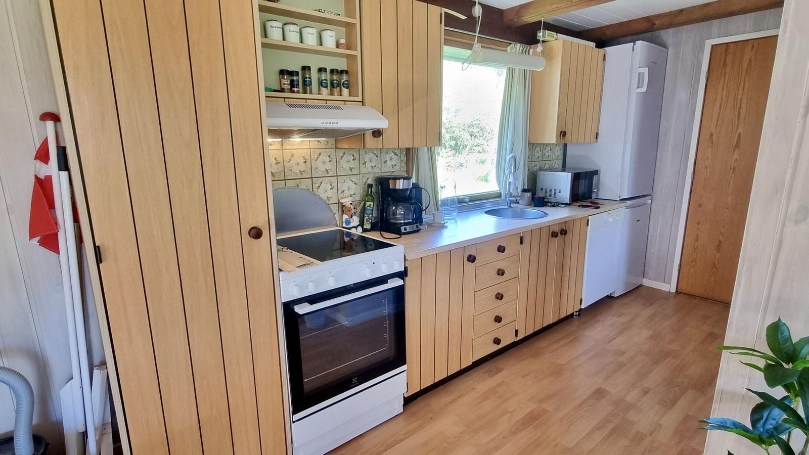 Küche mit Holzschränken, Herd, Kühlschrank und Fenster.
