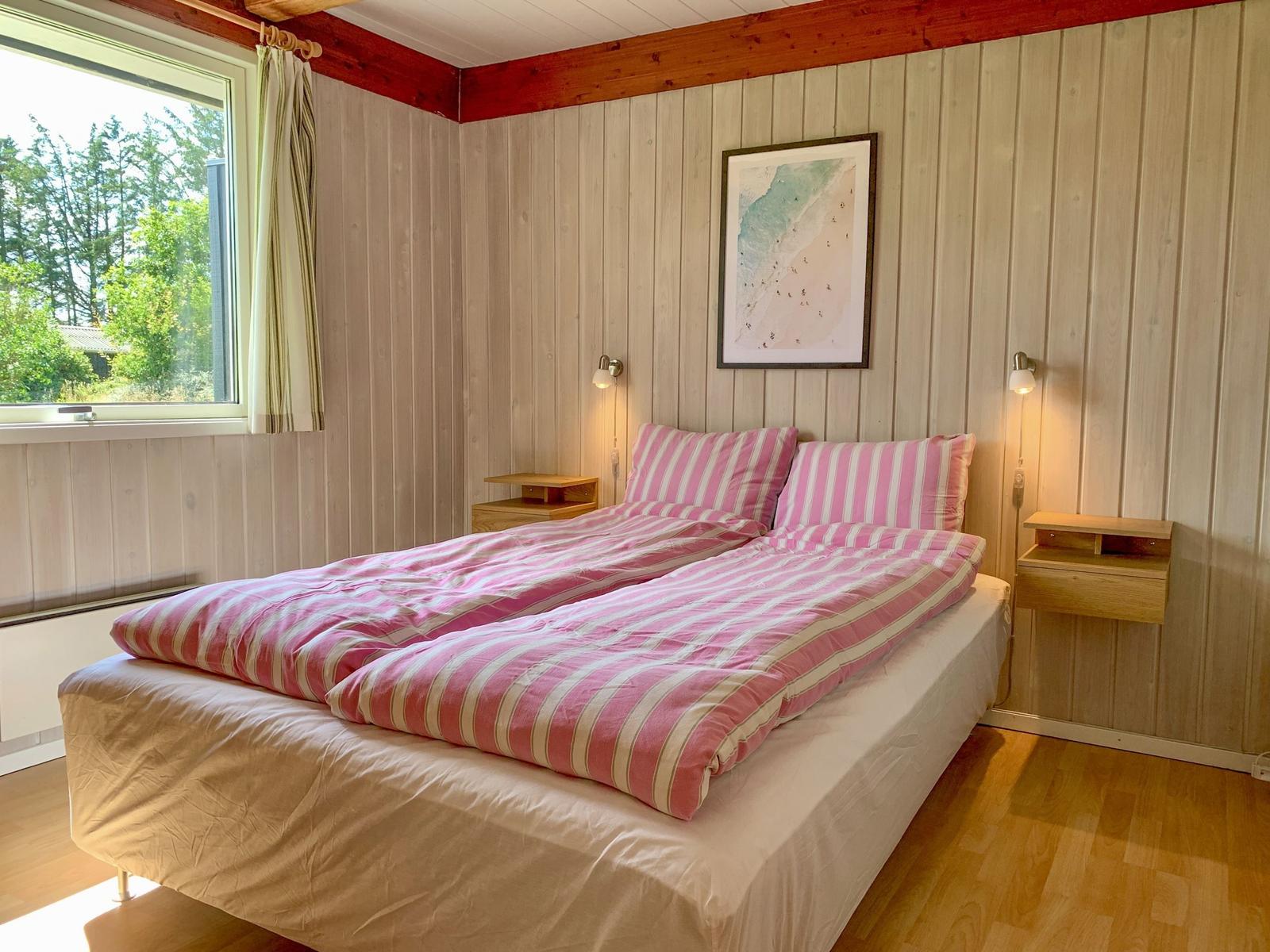 Schlafzimmer mit Doppelbett, Holzwand und Fensterblick auf Wald.