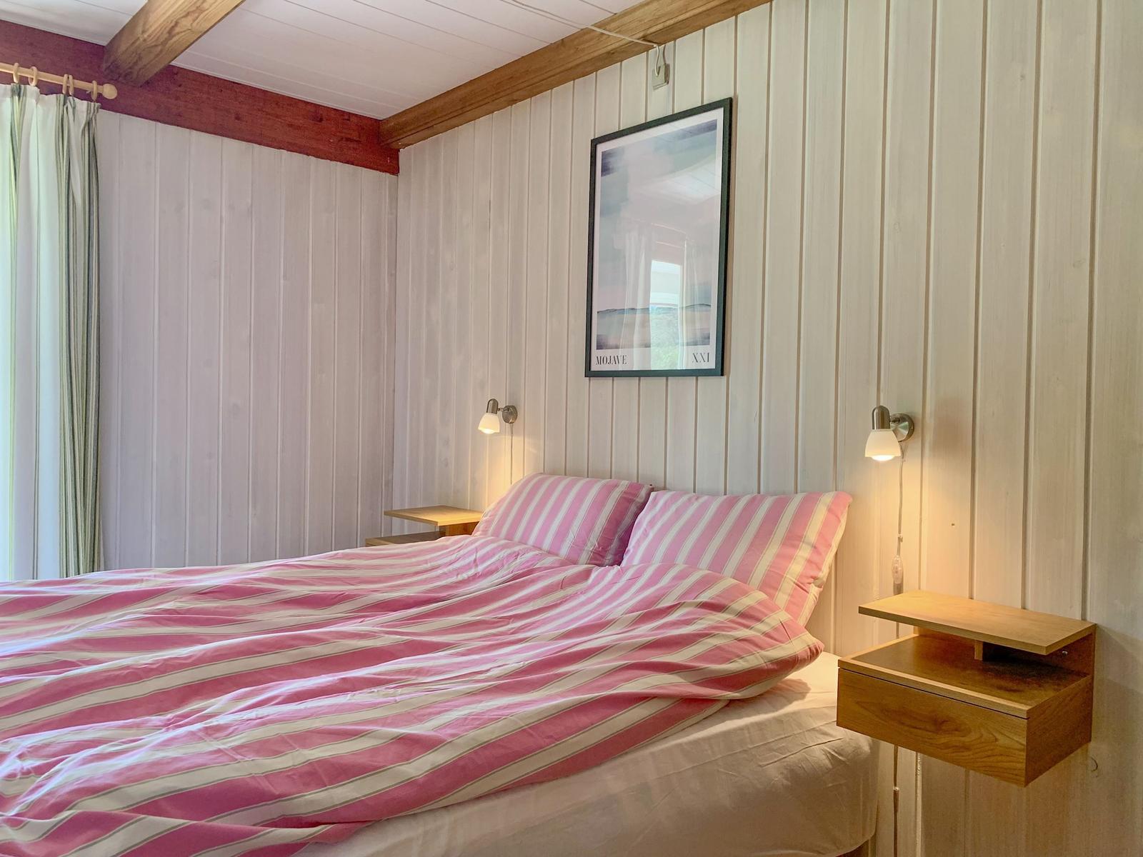Schlafzimmer mit Bett, rosa Bettwäsche, Holzwand und Wandlampen.