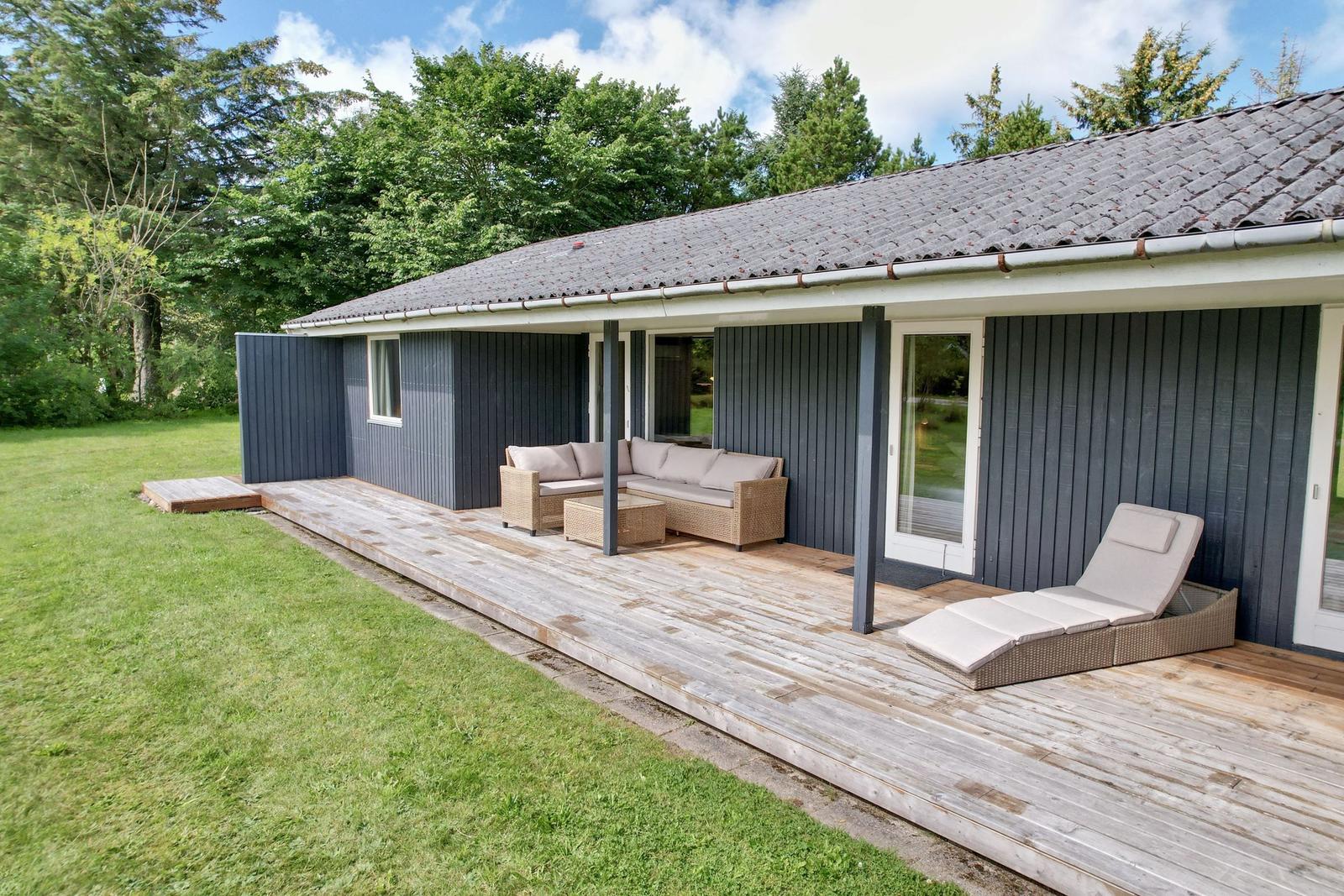 Terrasse mit Sitzgruppe und Liegestuhl neben Haus mit Holzdecke und grünem Rasen.