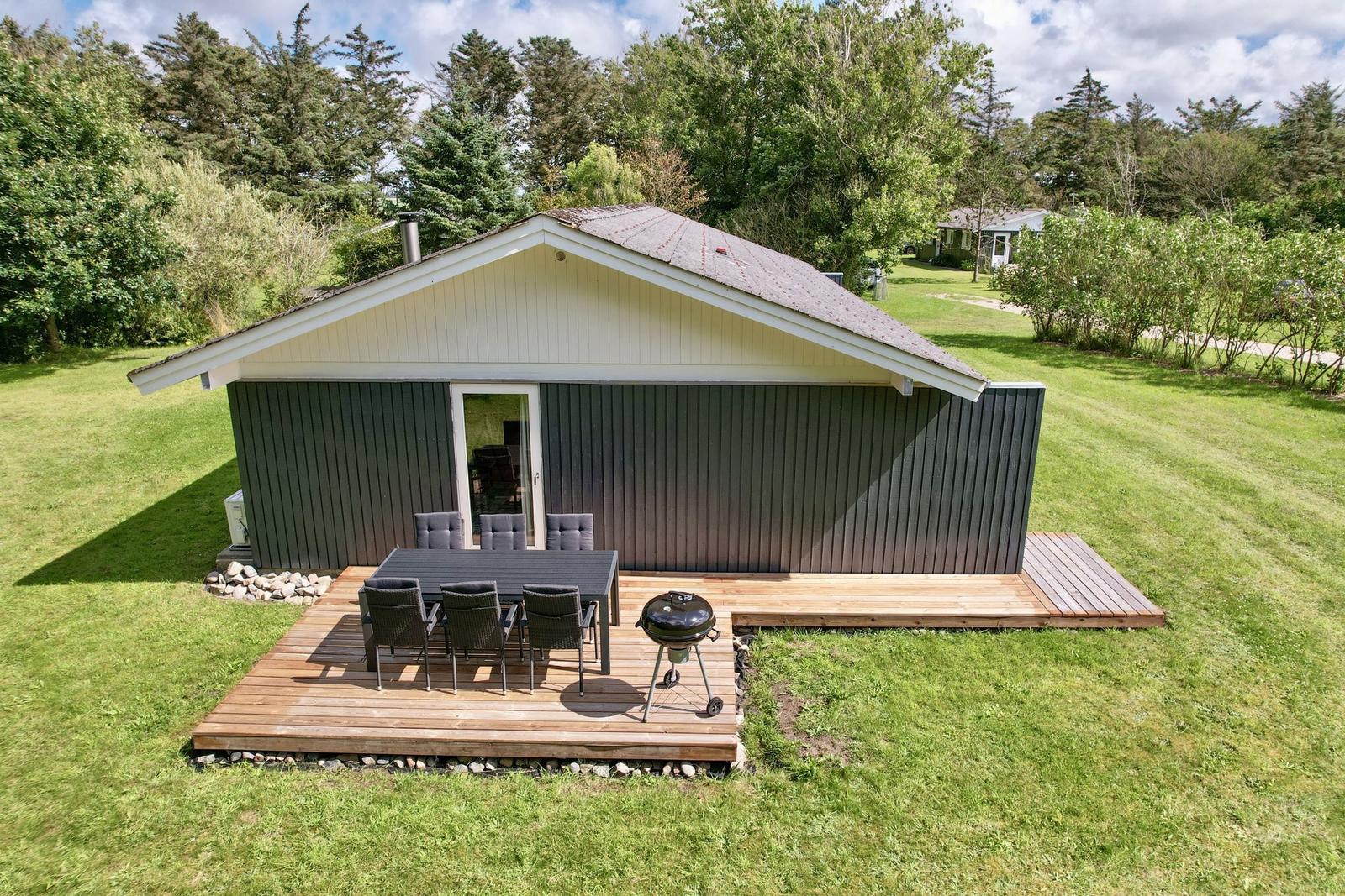 Holzhütte mit Terrasse, Grill und Garten. Tisch und Stühle für Außensitzgelegenheit.