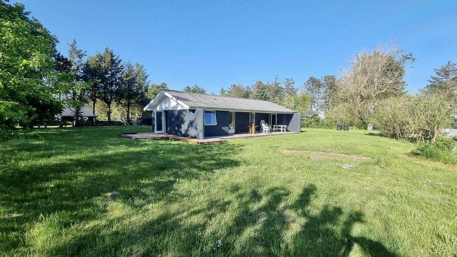 Moderne Hütte mit Terrasse und Garten. Umgeben von Bäumen und Gras.