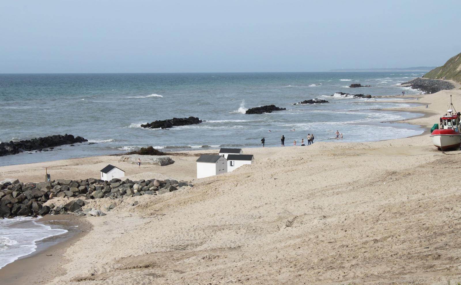 Strand mit weißen Hütten, Felsen und einem roten Boot.