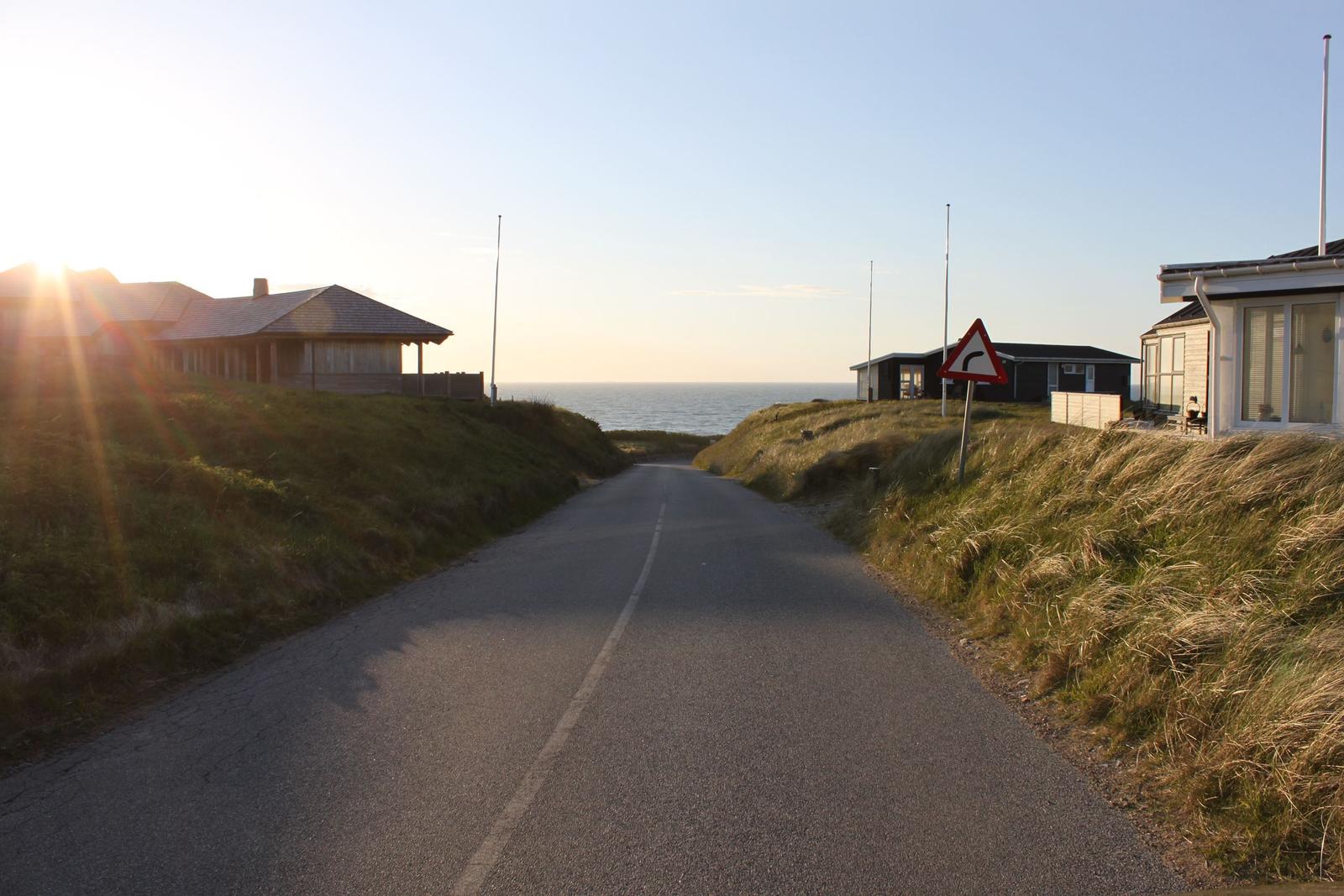 Straße entlang der Küste mit Häusern und Warnschild