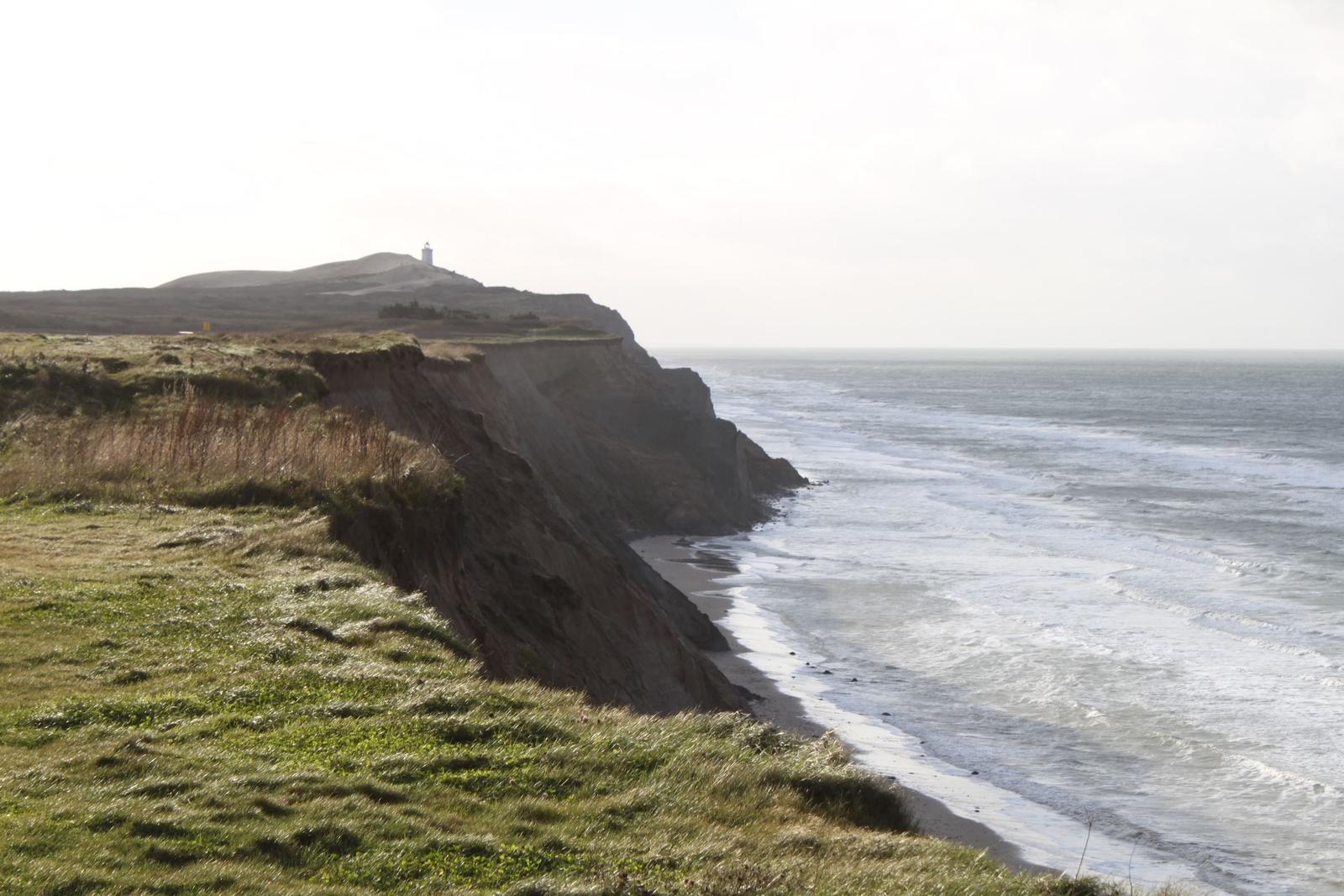 Meer an der Klippe mit Leuchtturm im Hintergrund.
