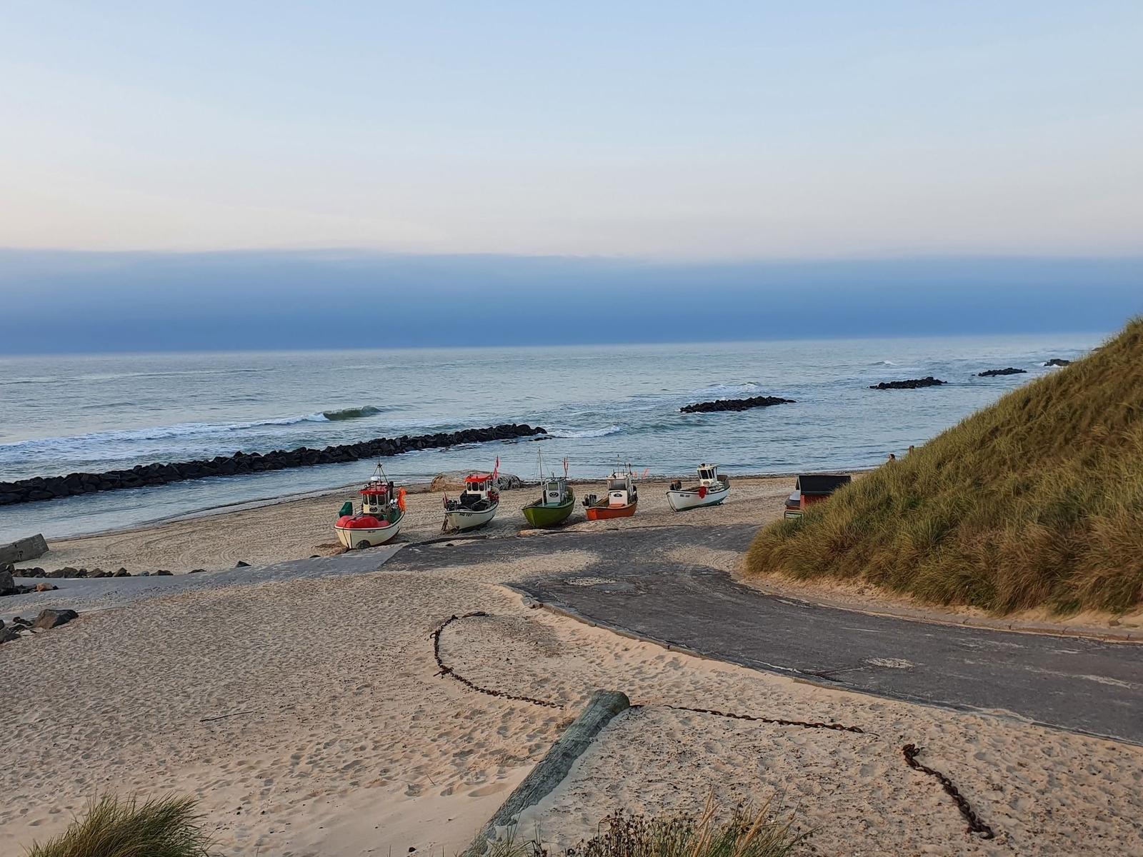 Strand mit Fischerbooten und Dünen im Hintergrund.