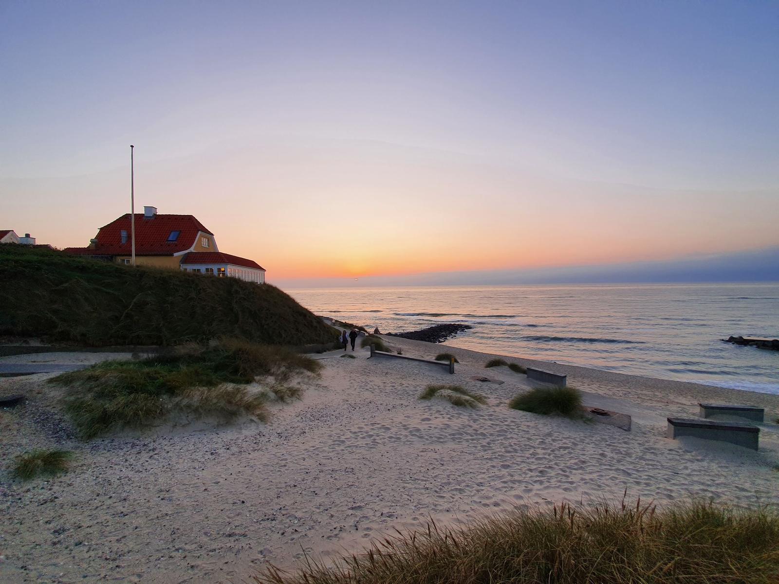 Haus mit rotem Dach auf Dünen über Strand bei Sonnenuntergang