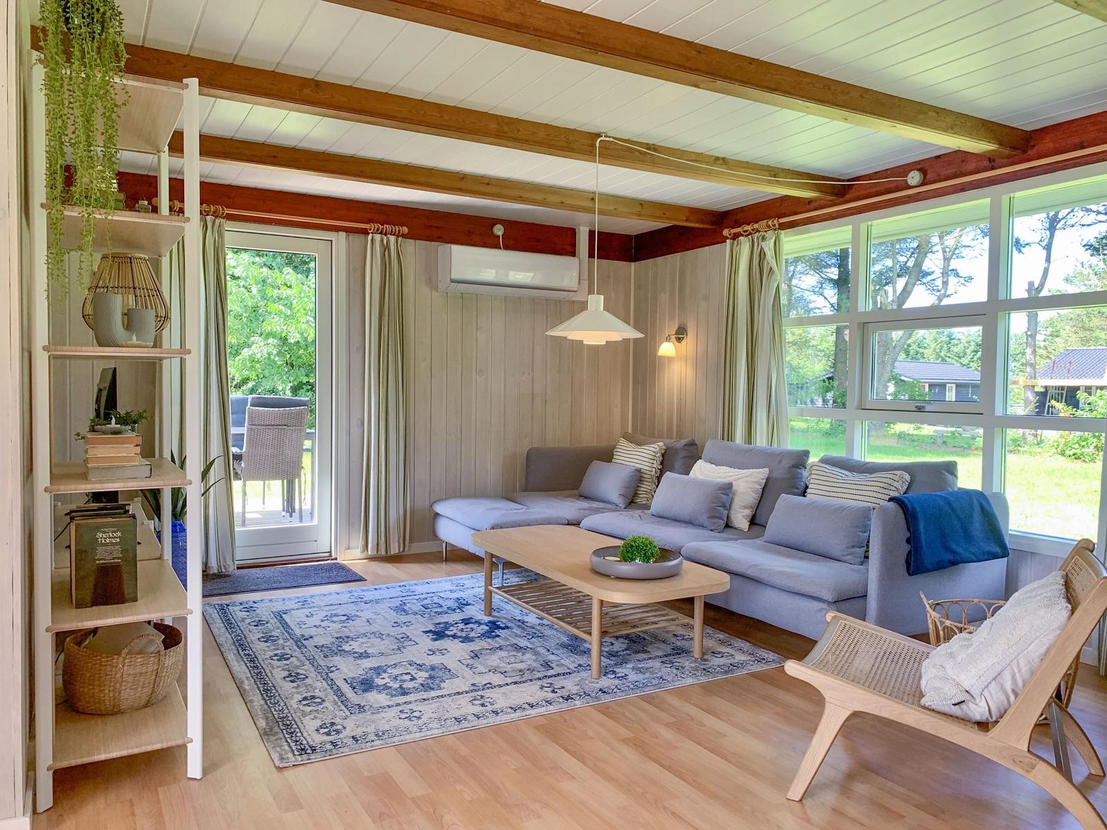 Wohnzimmer mit Sofa, Tisch und Teppich. Holzdecke und große Fenster.