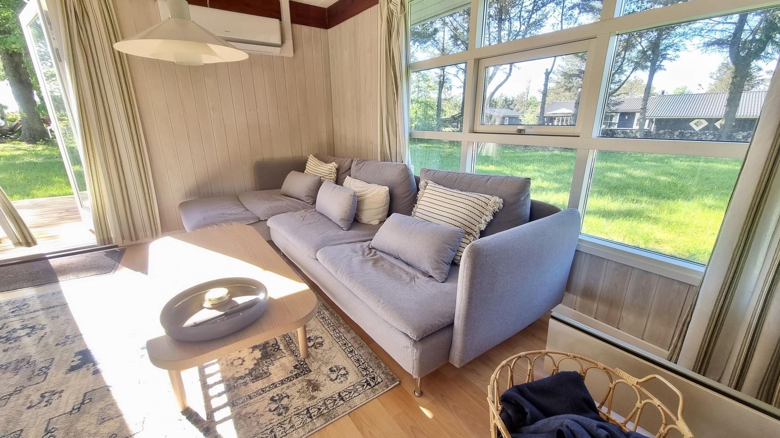 Wohnzimmer mit Sofa, Tisch und Blick auf Grünflächen.