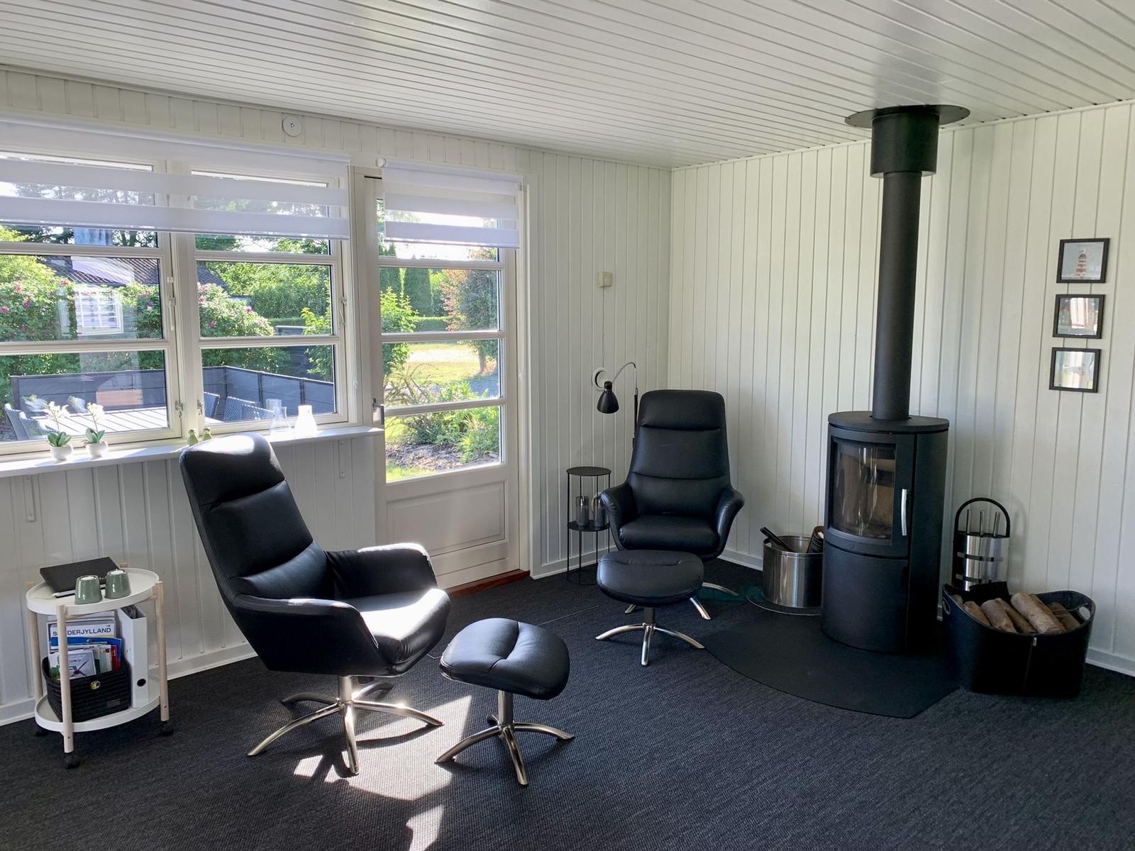 Zimmer mit zwei schwarzen Sesseln, Kamin und Fenstern zum Garten.