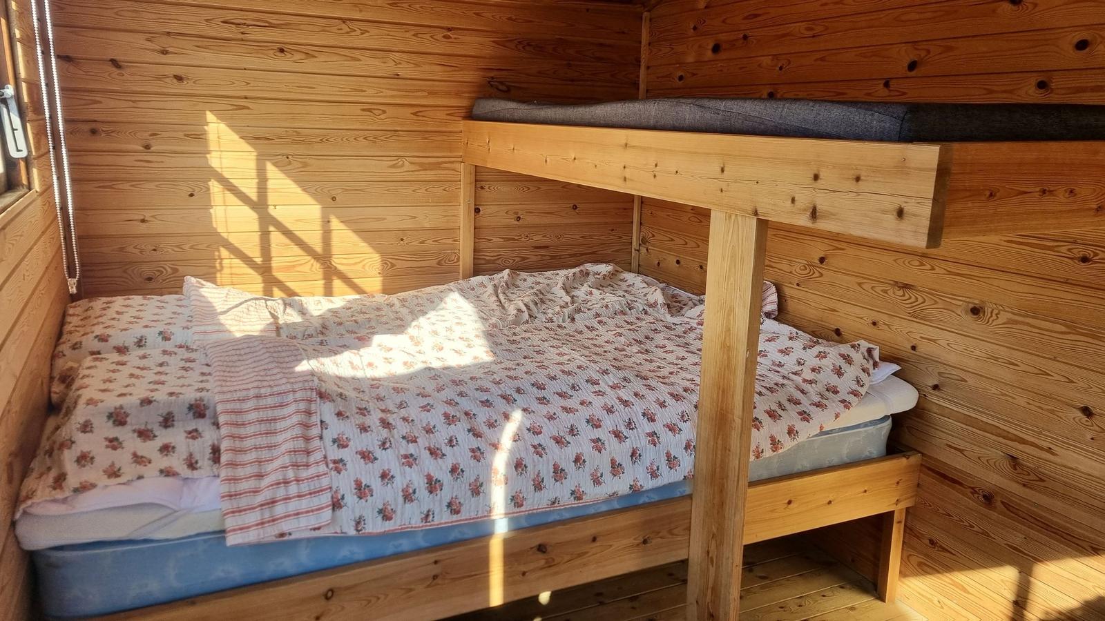Ein Schlafzimmer mit Holzwand und Doppelbett. Oben liegt ein Matratzenkissen.