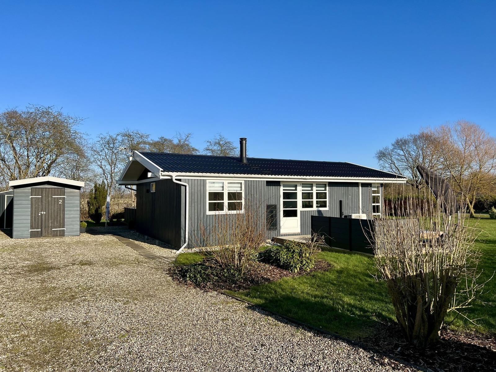 Moderne Holzhütte mit Garten und Garage. Klarer Himmel und Bäume im Hintergrund.
