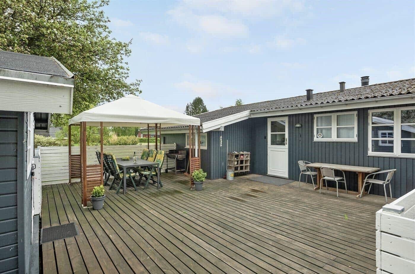 Terrasse mit Tisch, Stühlen und Sonnenschutz neben blauem Haus.