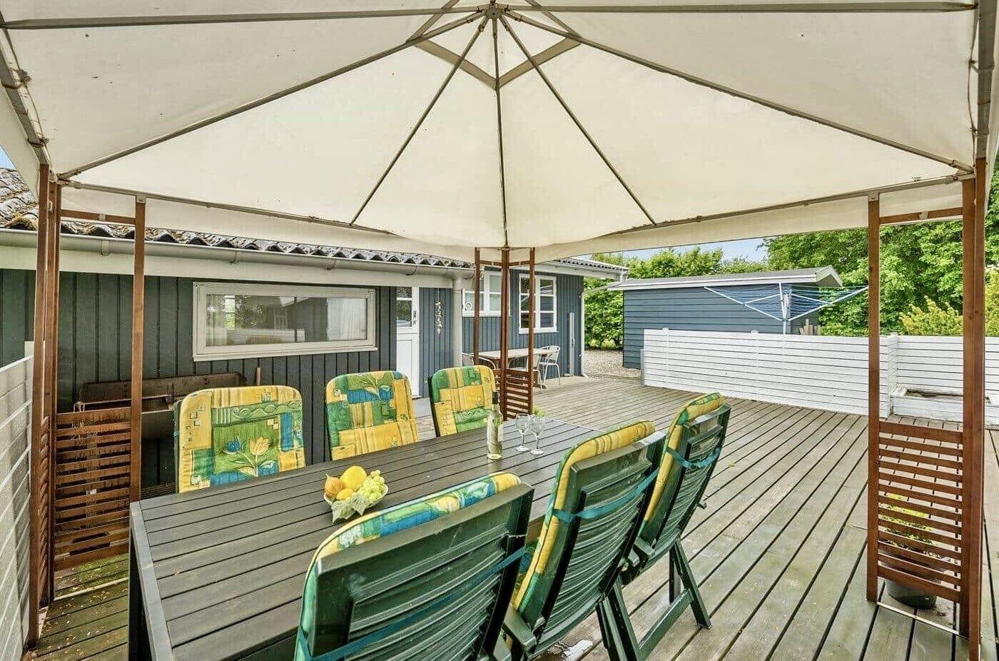Terrasse mit Tisch, Stühlen und Sonnenschutz. Hintergrund: Haus und Grün.