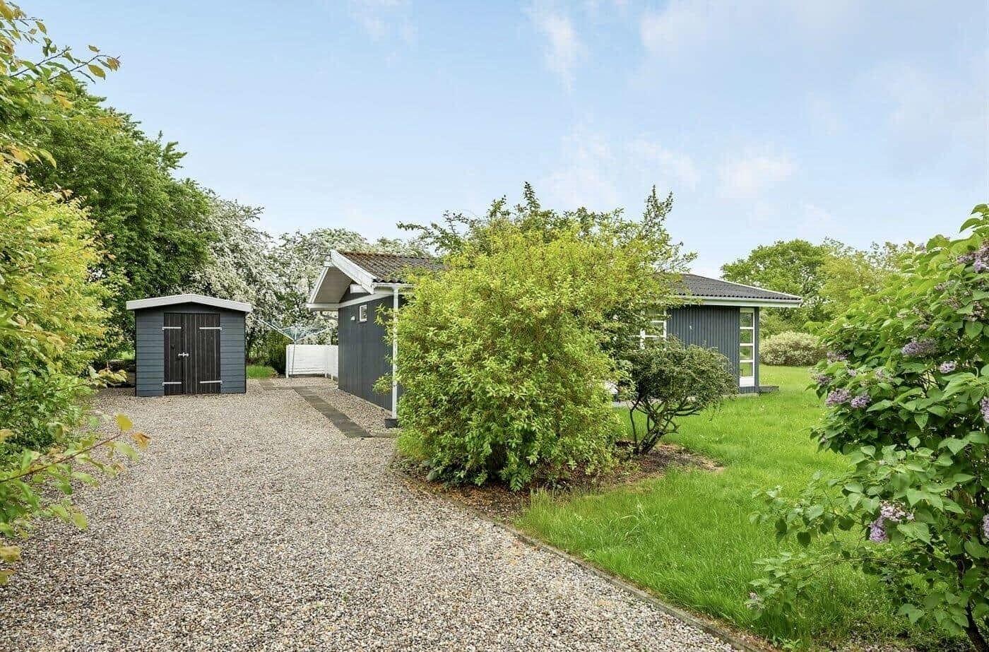 Haus mit Garten, Schuppen und Kiesweg unter blauem Himmel.