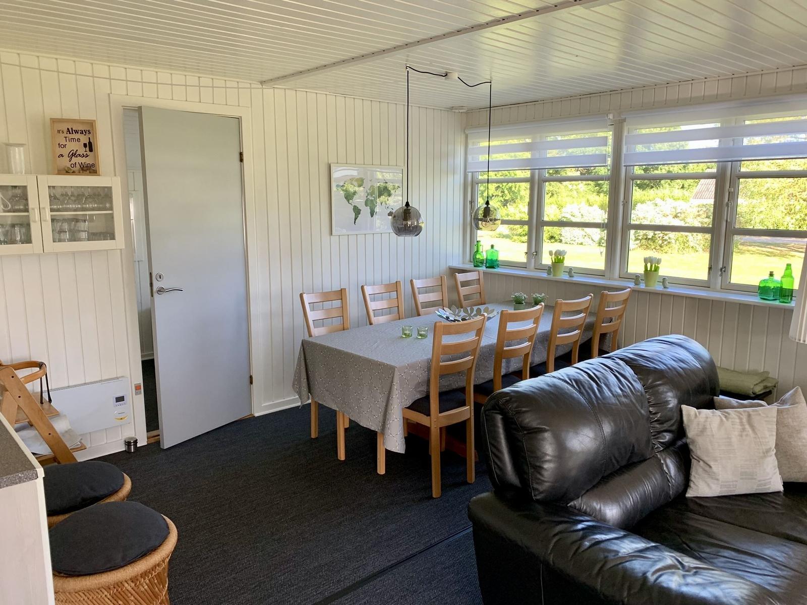 Essbereich mit Tisch, Stühlen und Sofa. Große Fenster mit Blick auf Garten.