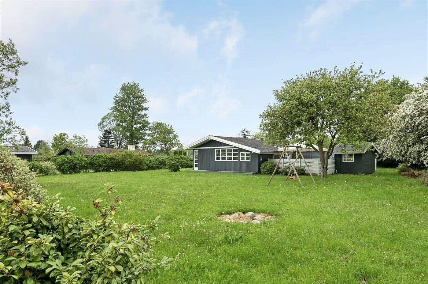 Ein graues Haus mit großem Garten und Schaukel unter Bäumen.