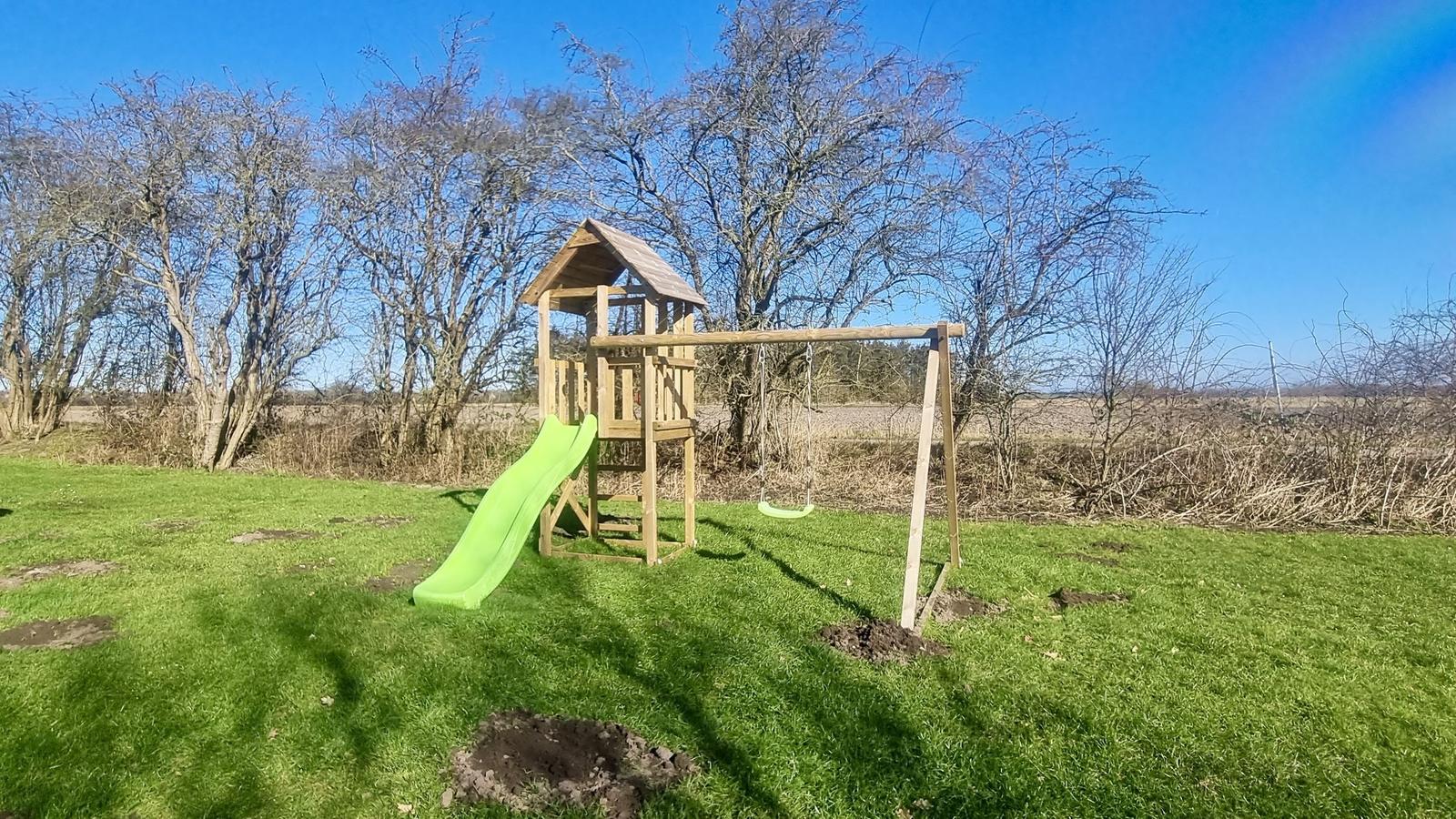 Holzspielplatz mit Rutsche und Schaukel auf grünem Rasen