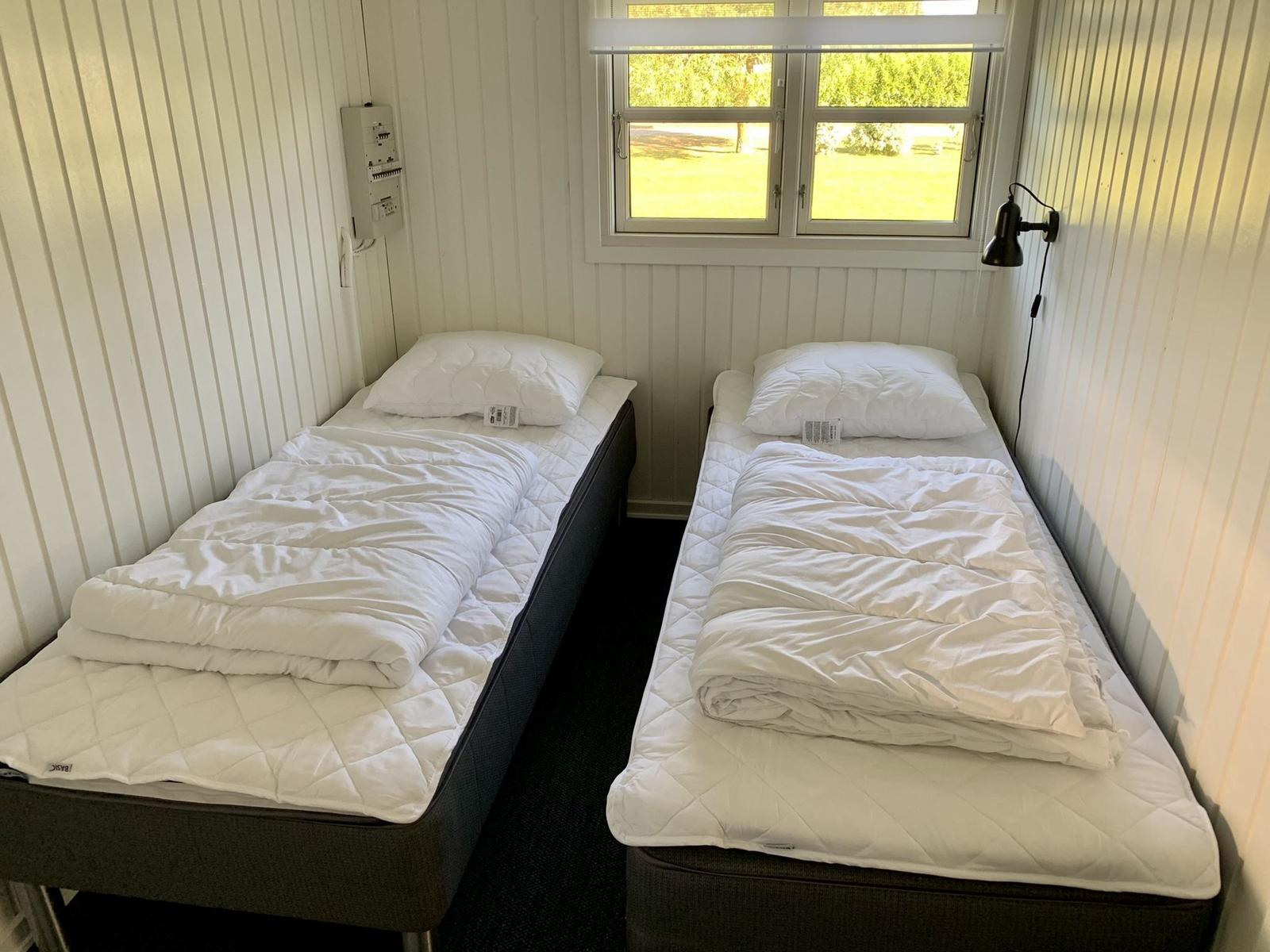 Zwei Betten mit weißen Bettwäschen und Decken. Fenster mit Blick auf Grünfläche.