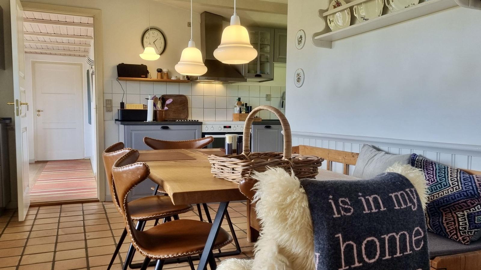 Essbereich mit Holztisch, Ledersitzen und Korb. Küche mit Arbeitsplatte und Dunstabzug.