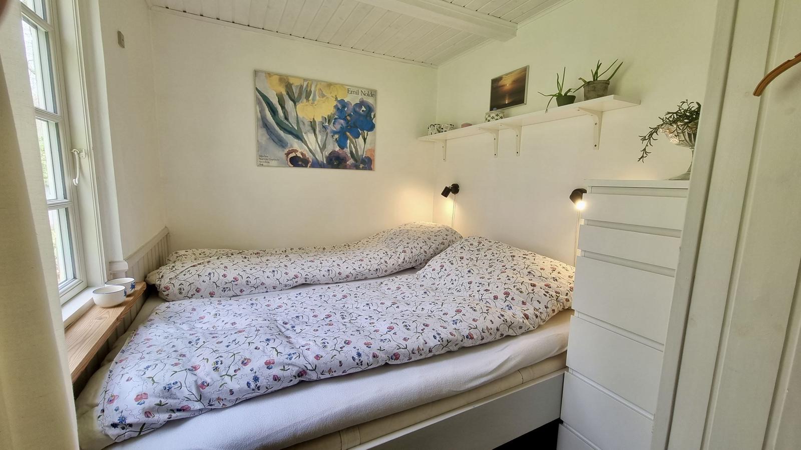 Schlafzimmer mit Bett, Fenster, Wandbild und weißen Regalen.