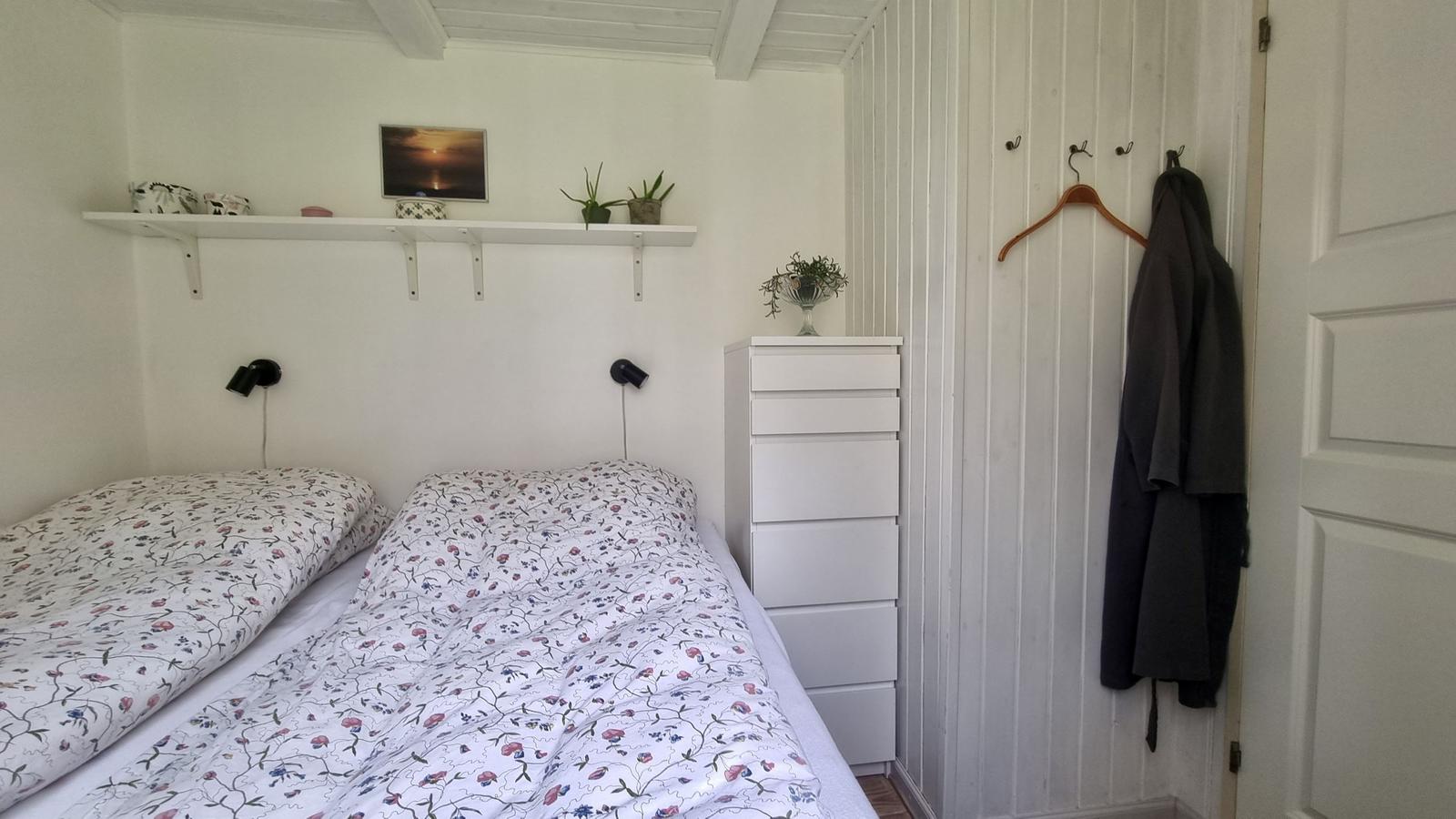 Schlafzimmer mit Doppelbett, weißen Wänden und einem Kleiderschrank.